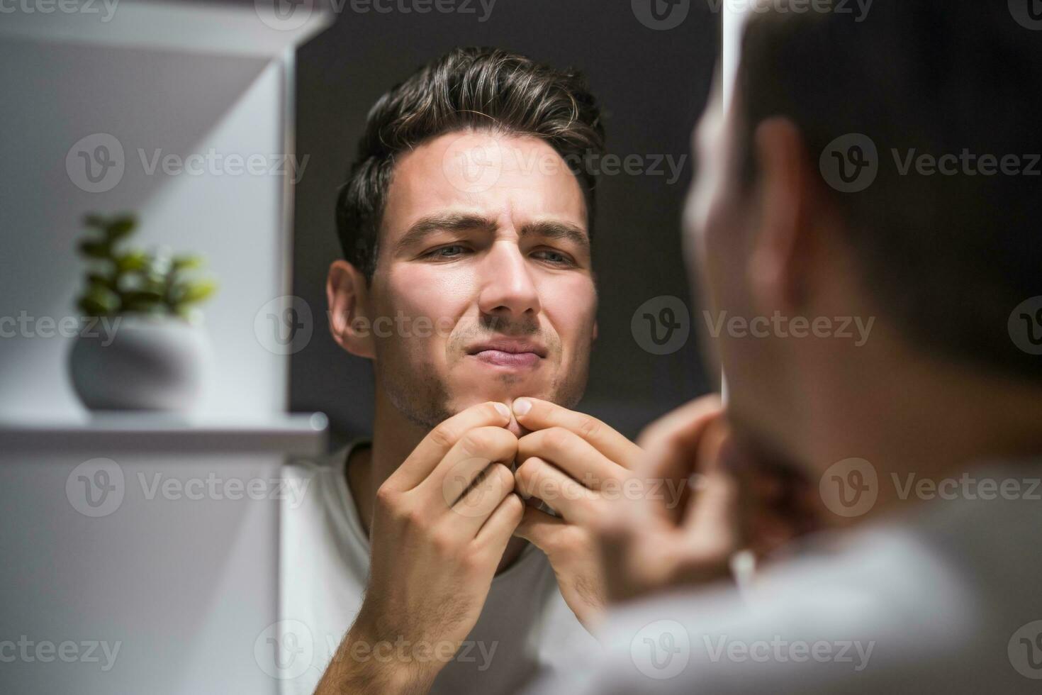 Man squeezing pimple while looking himself in the mirror photo