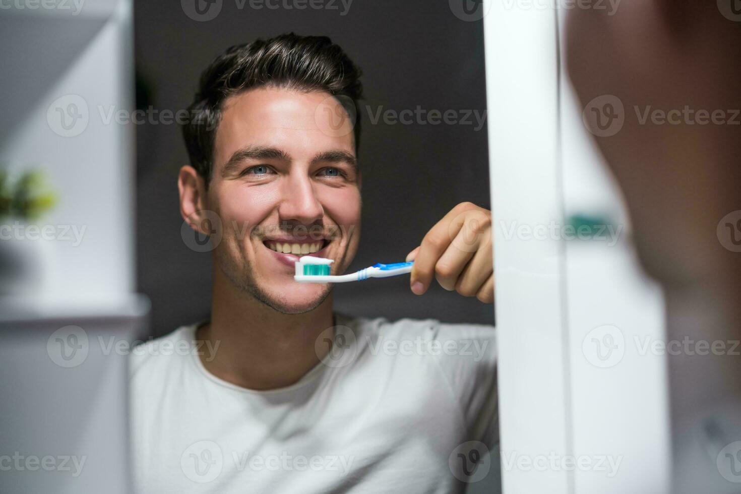 Man is brushing teeth while looking himself in the mirror photo