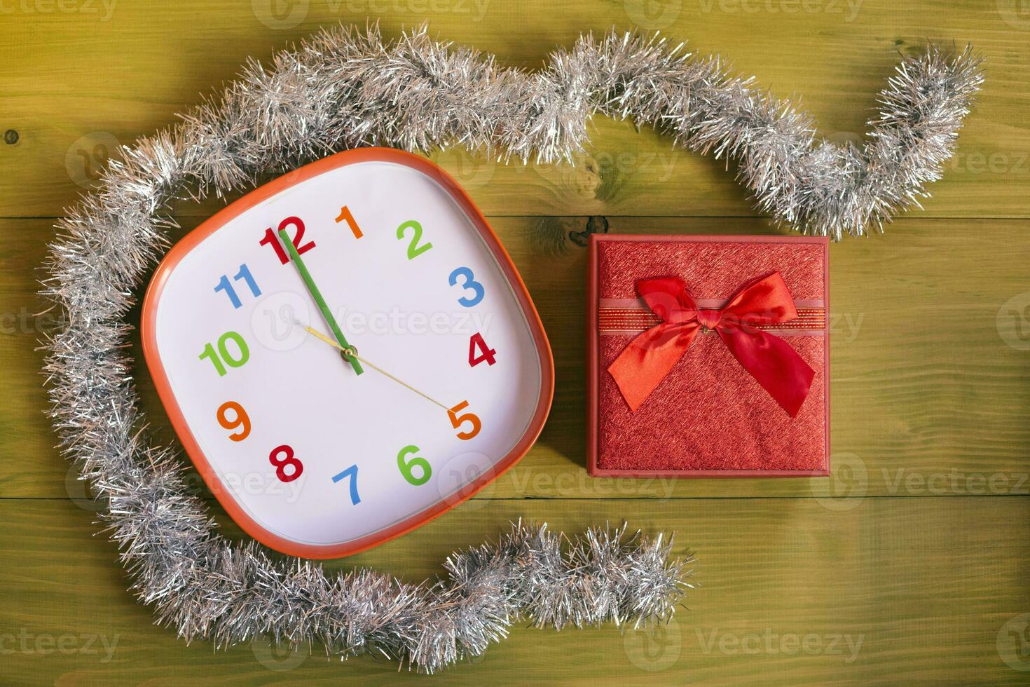 Image of decorated clock showing midnight and gift in beautiful red box on wooden table photo