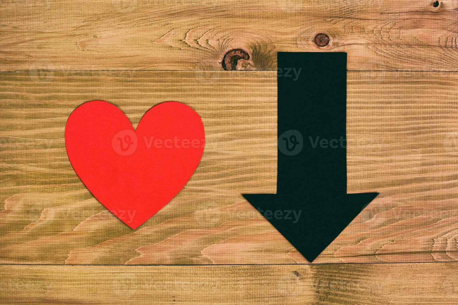 Red heart and arrow going down on wooden table, relationship breakup concept. photo