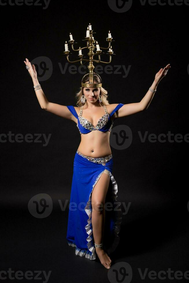 Beautiful belly dancer performing belly dance with candle holder on black background photo