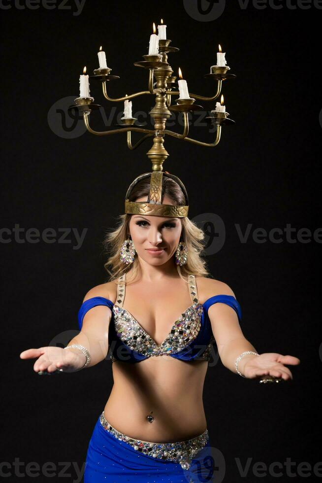 Beautiful belly dancer performing belly dance with candle holder on black background photo