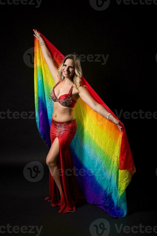 Beautiful belly dancer holding veil and performing belly dance on black background photo