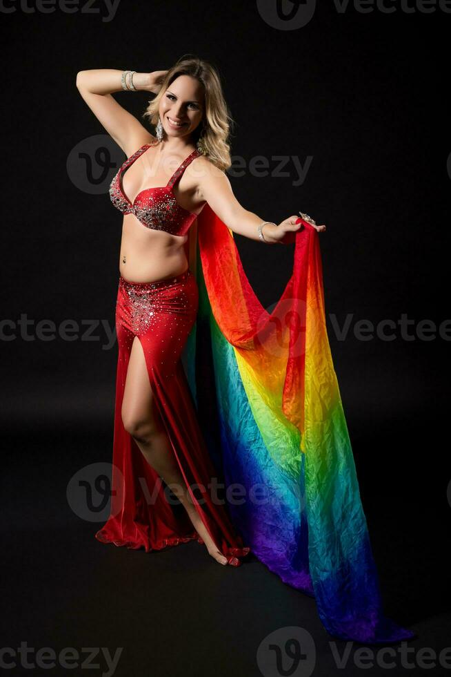 Beautiful belly dancer holding veil and performing belly dance on black background photo