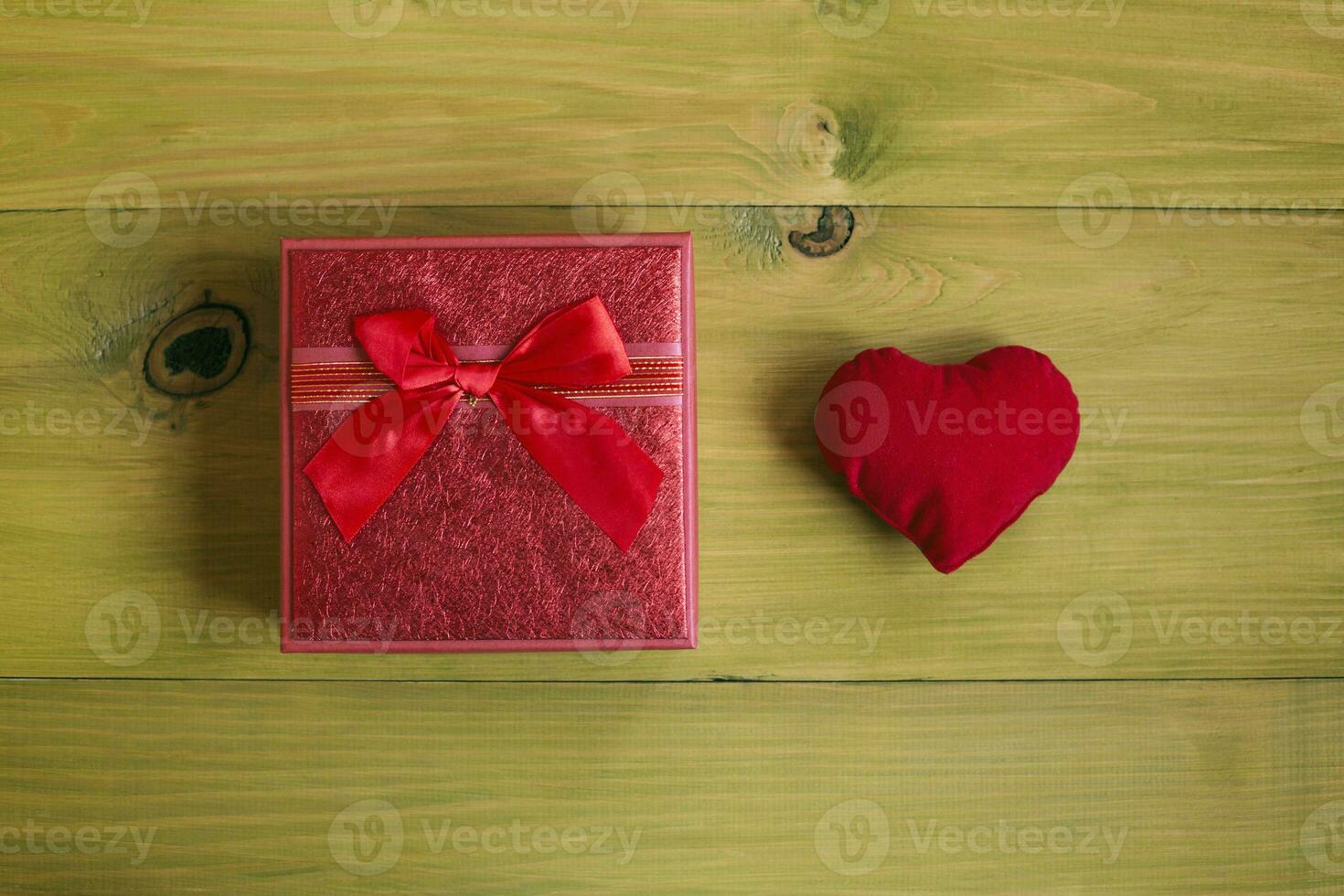 Red gift box with red ribbon and heart on wooden background photo