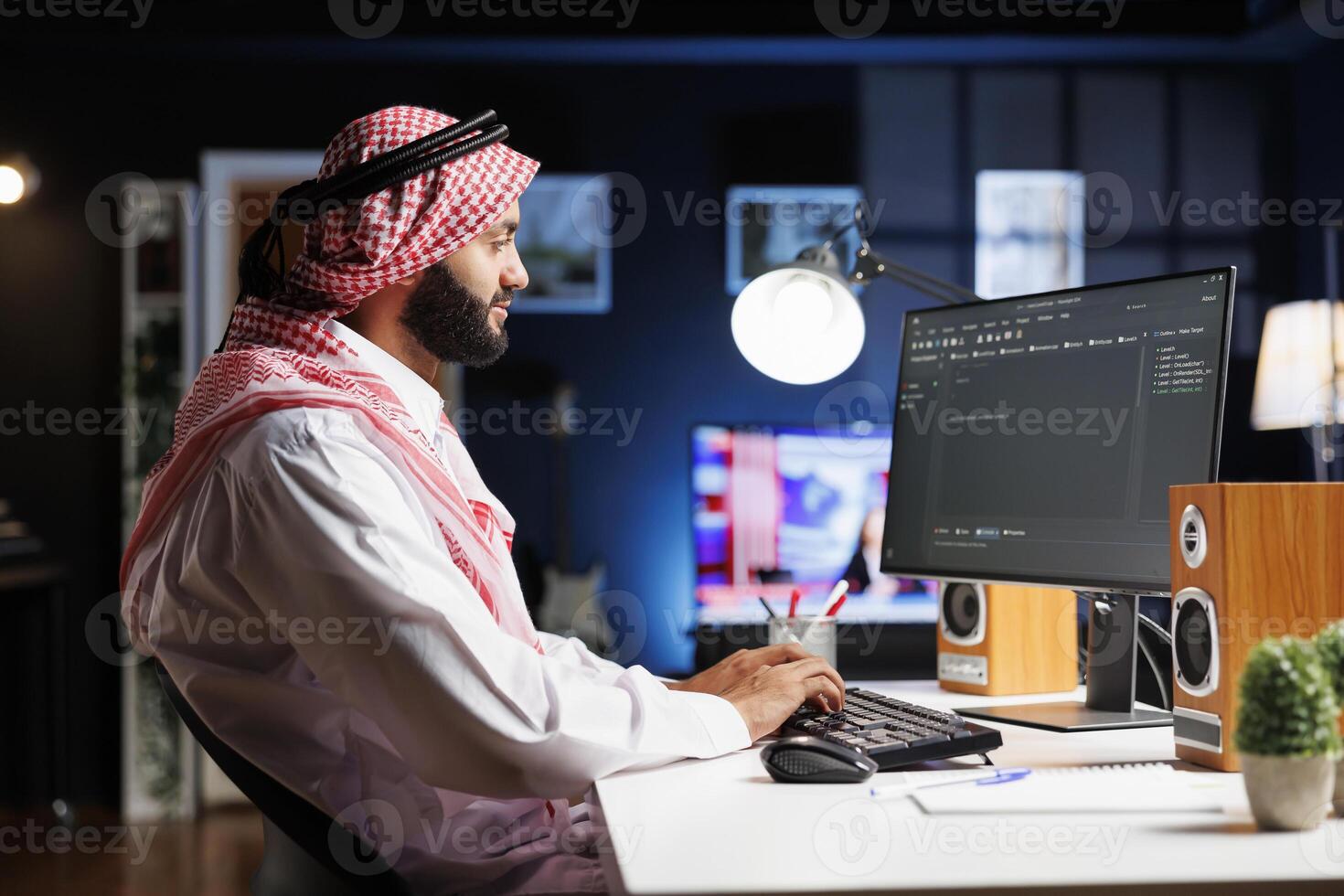 Image shows an Arab software developer working at the pc monitor, seated at a workstation processing algorithm. Muslim Coder uses a desktop computer to work on the user interface. photo