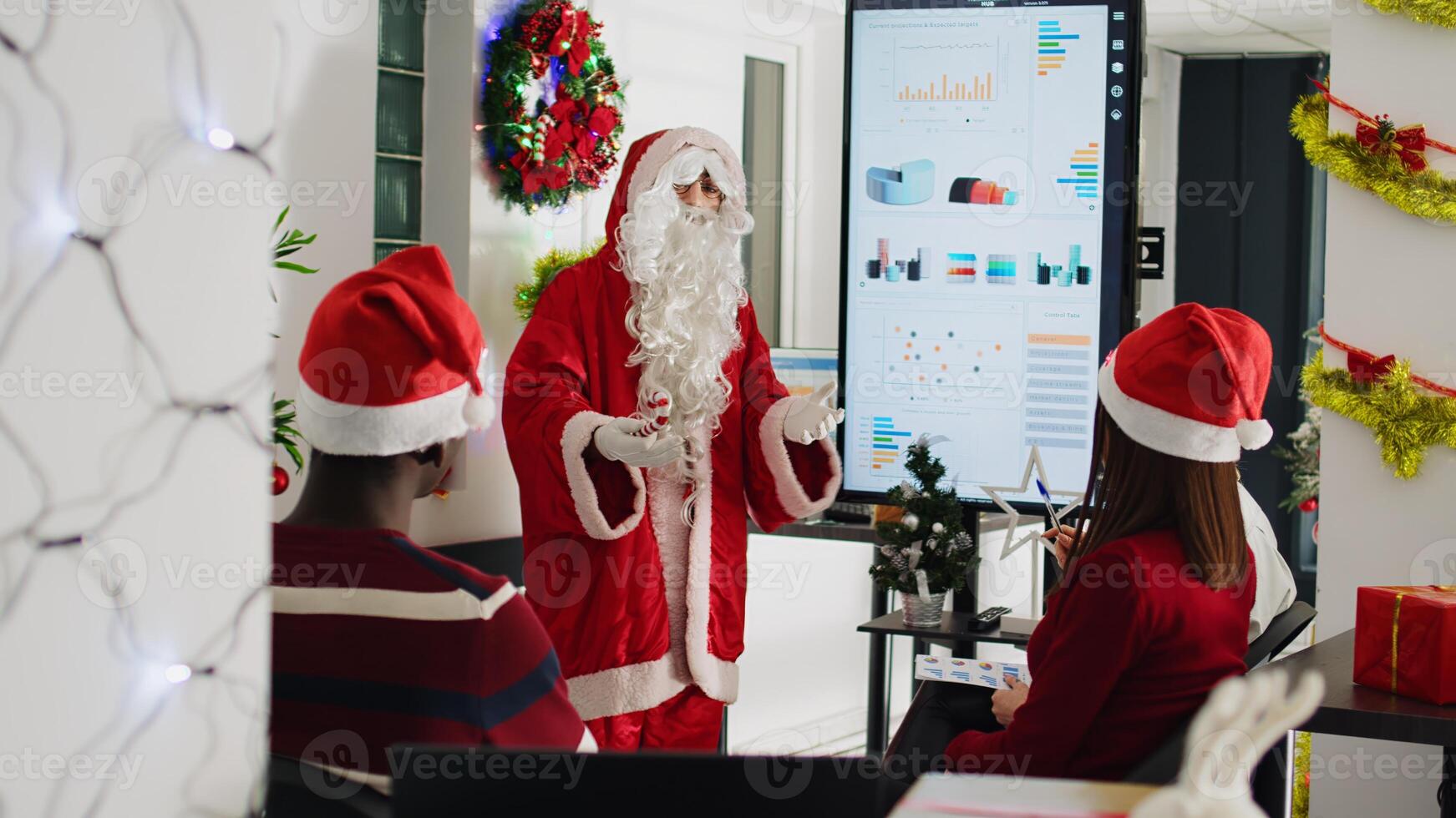 Licensed orator dressed as Santa Claus doing presentation in front of company workers using candy cane pointer. Staff learning how to advance their career during meeting in Christmas ornate office photo
