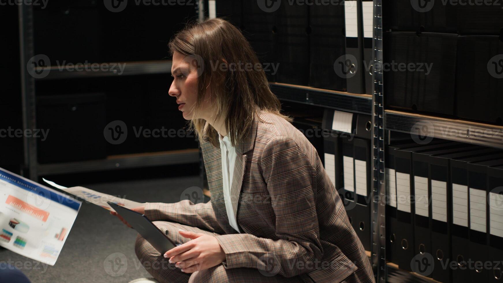 African american detective and caucasian police officer researching clues and evidence while sitting on floor in incident room. Female inspector with laptop discussing criminal case with policeman. photo