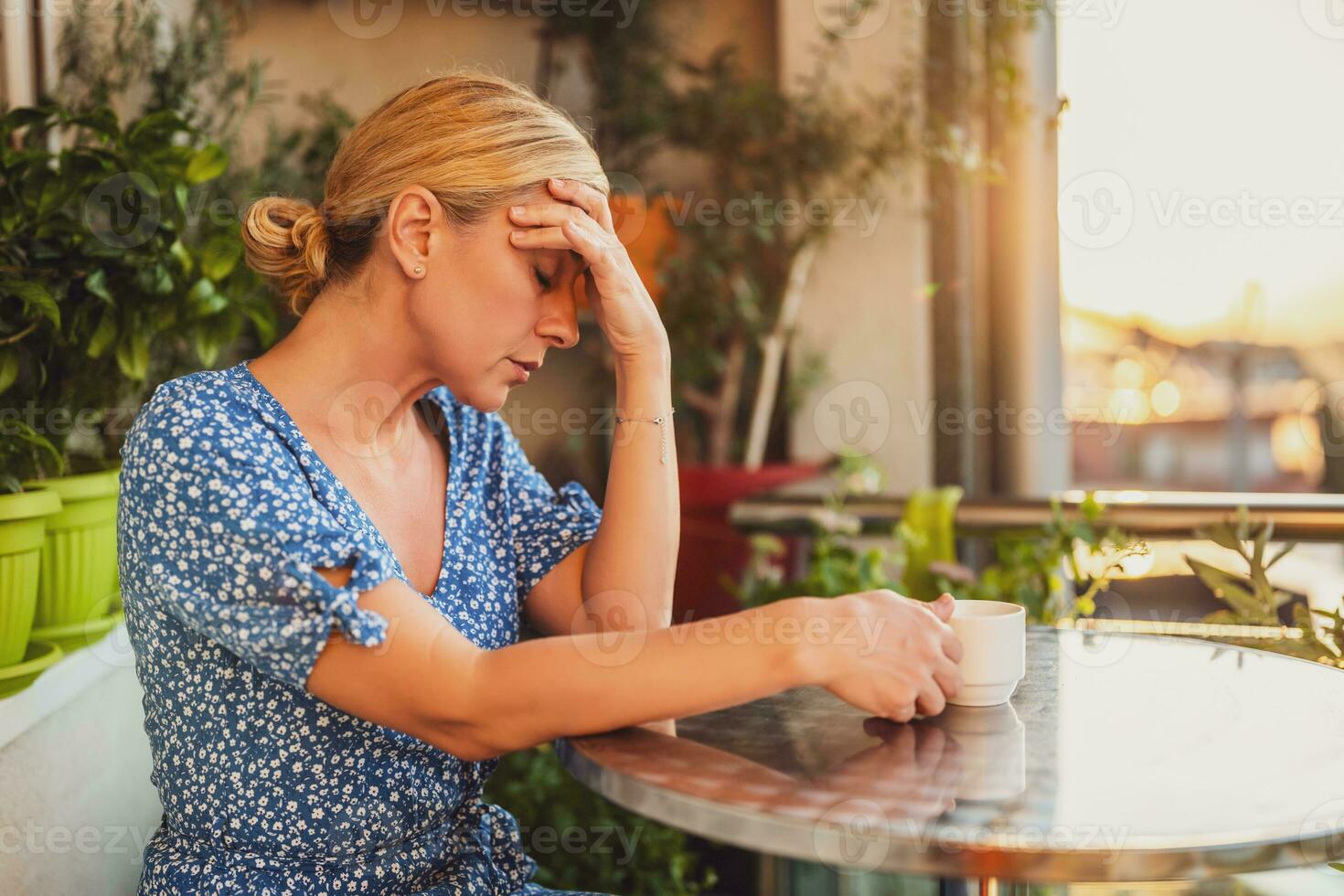 Sad woman having a headache and drinking coffee while sitting on her