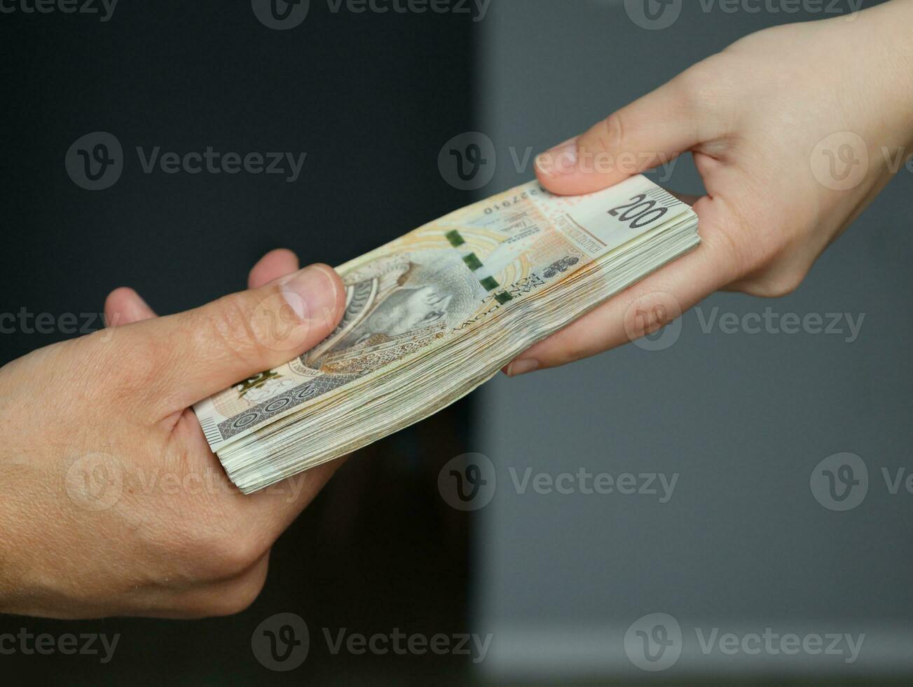 male hand giving a bundle of large banknotes to female hands. selective focus photo