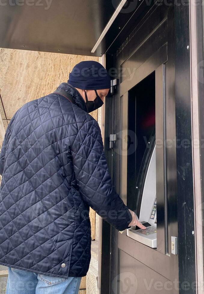 man in a black mask and a disposable glove uses an ATM. selective focus photo