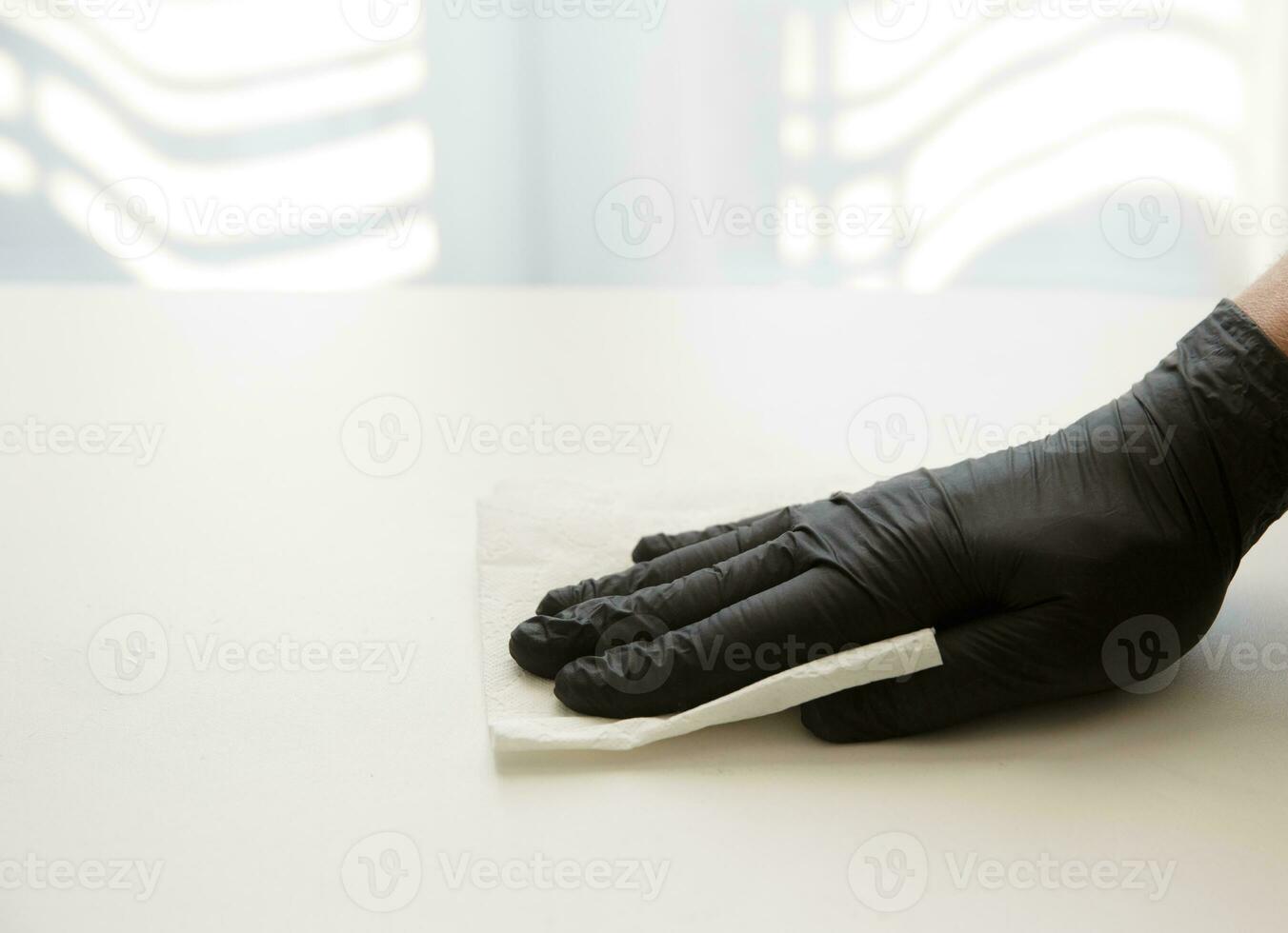 hand in a black nitrile glove wipes the table with disinfectant solution. selective focus photo