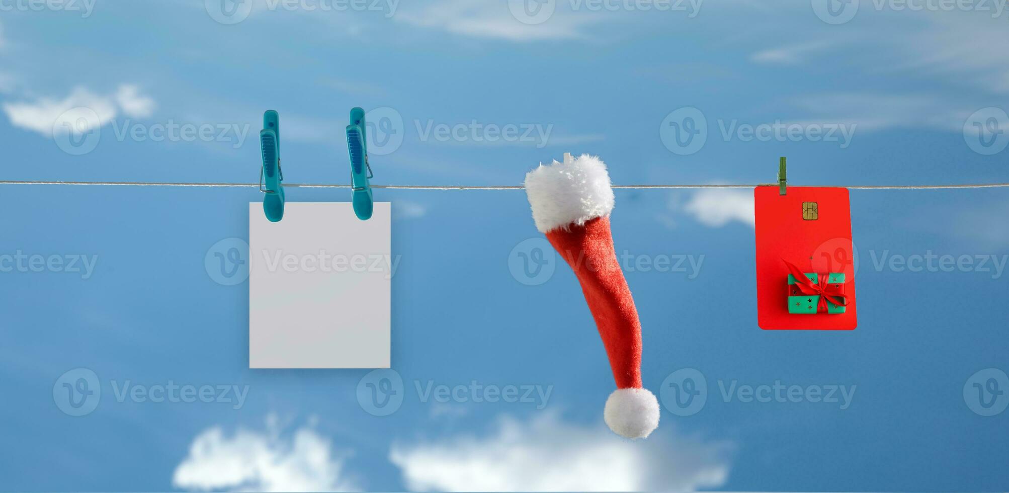 rope on which a plastic card, Santa hat and postcard hang against the blue sky. selective focus photo