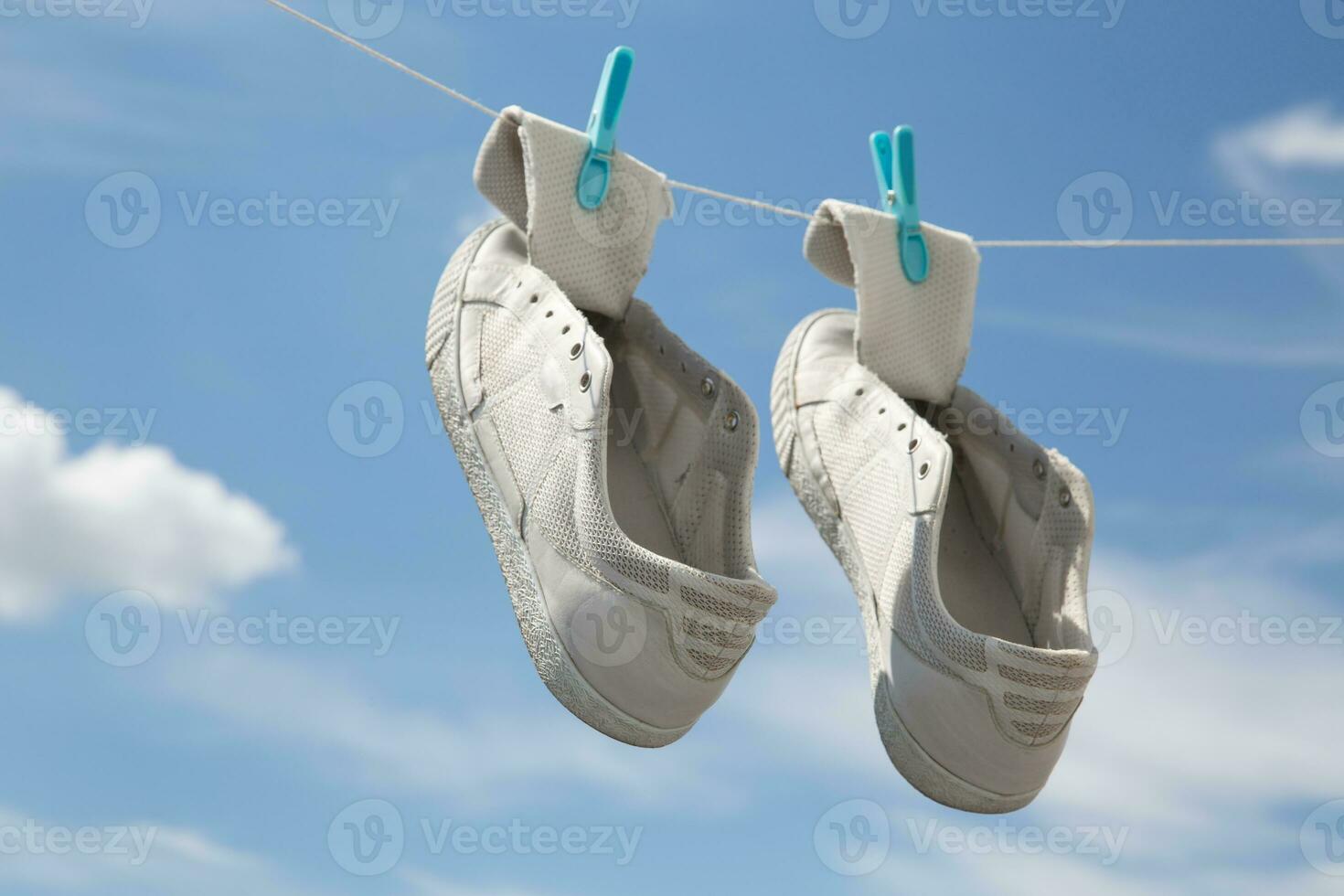 antiguo zapatillas seco en pinzas para la ropa en un cuerda en contra un antecedentes de azul cielo con nubes alto calidad foto