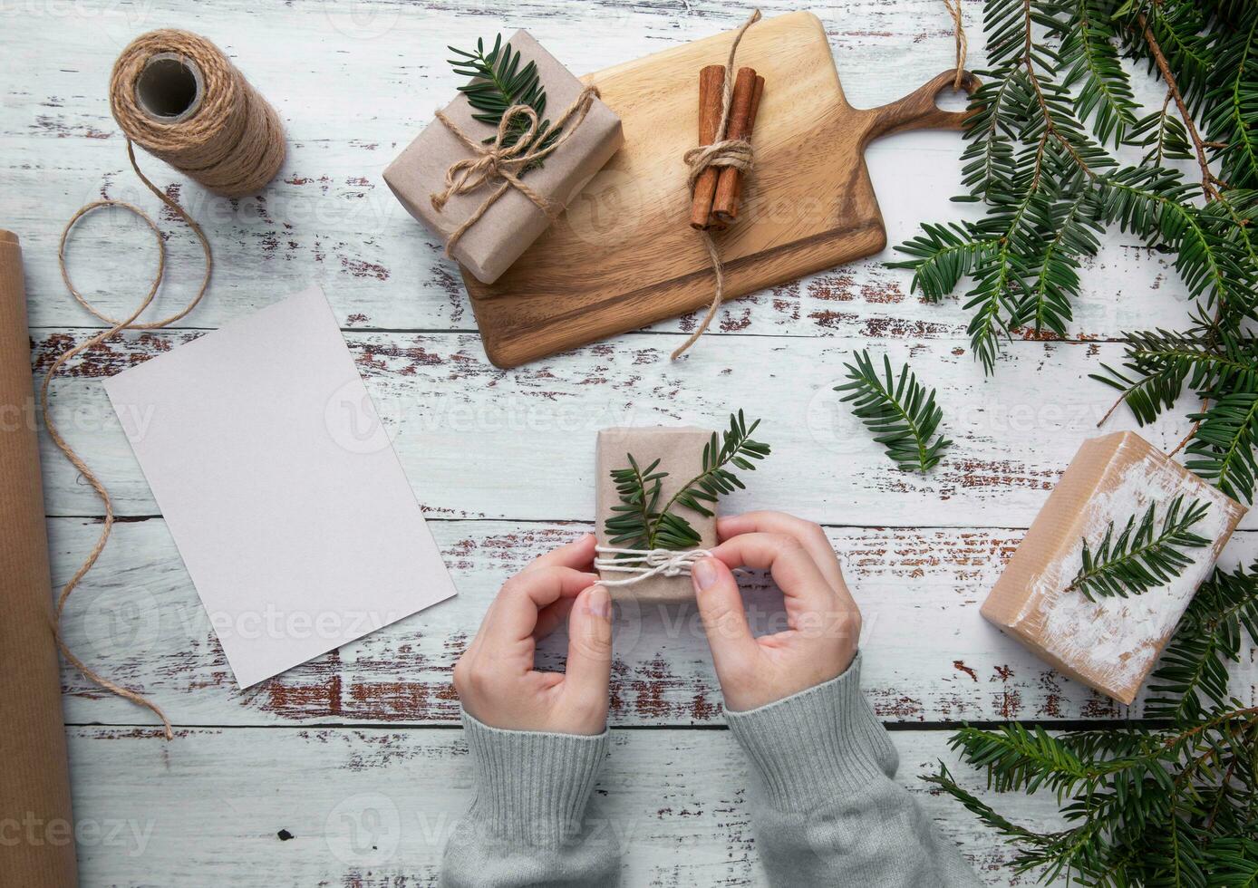 manos sostener Navidad regalo , abeto árbol ramas en blanco de madera mesa. alegre Navidad . plano laico , parte superior ver . Navidad tarjeta Bosquejo y canela blanco antecedentes foto