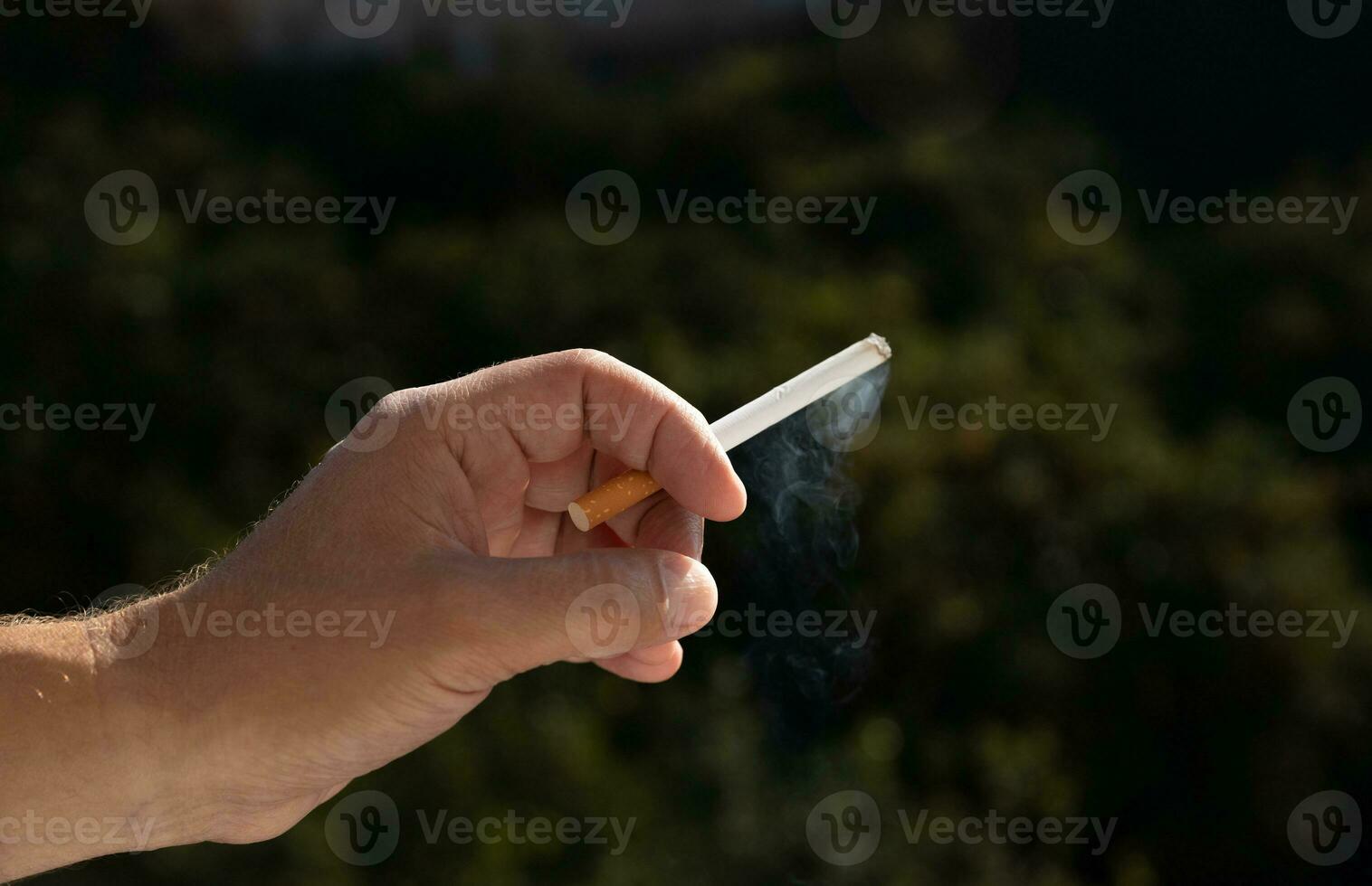 a cigarette in a man's hand against a background of green vegetation. close up. High quality photo