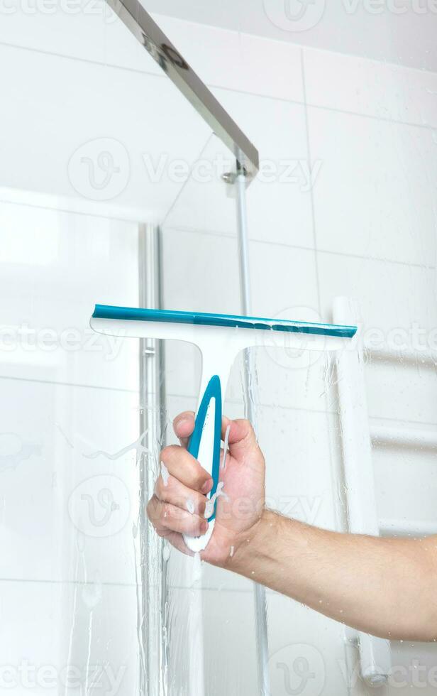 hand with glass scraper cleans glass in shower. High quality photo