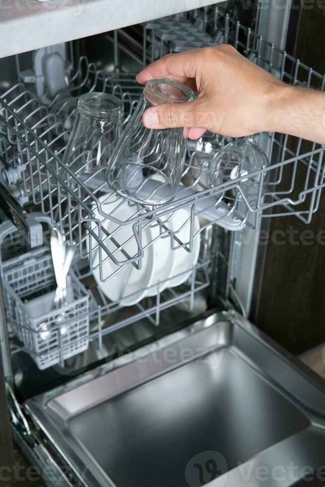 Housework open dishwasher and man putting a glass in the machine. High quality photo