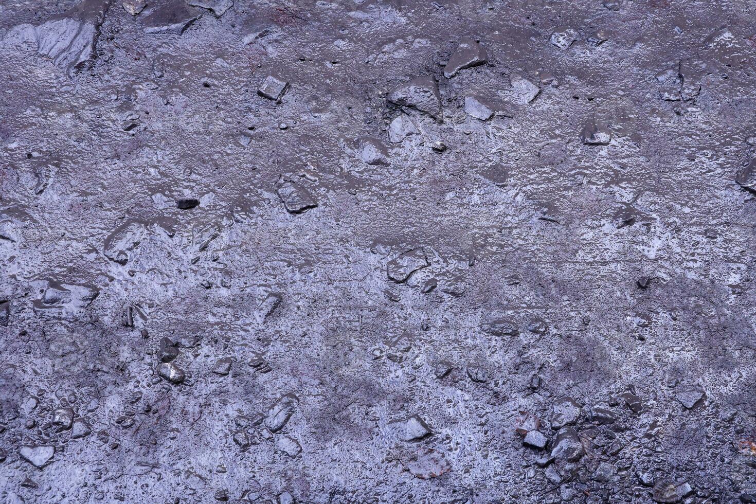 Close up of muddy puddle with small stones on wet surface. Background texture with top view photo