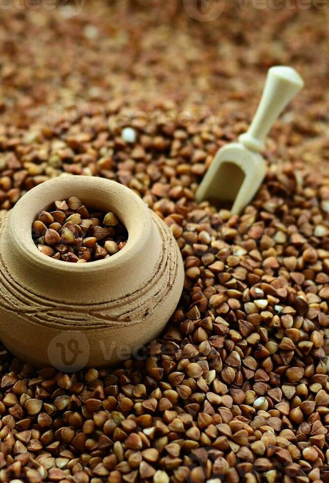 Background image of a large pile of buckwheat, in the middle of which lies a small jug and a wooden spatula for cereals photo