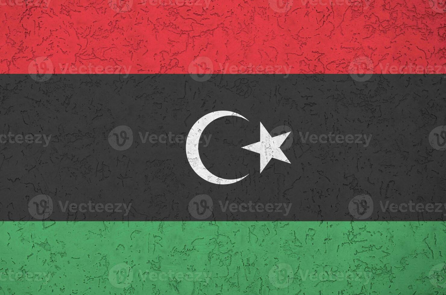 Libya flag depicted in bright paint colors on old relief plastering wall. Textured banner on rough background photo