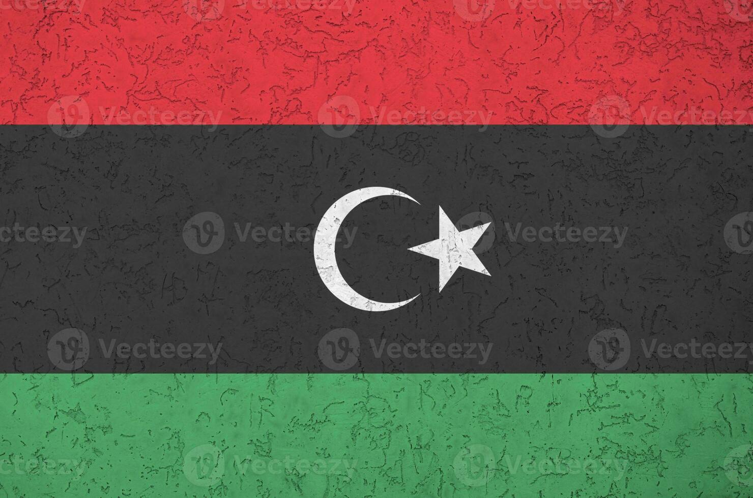 Libya flag depicted in bright paint colors on old relief plastering wall. Textured banner on rough background photo