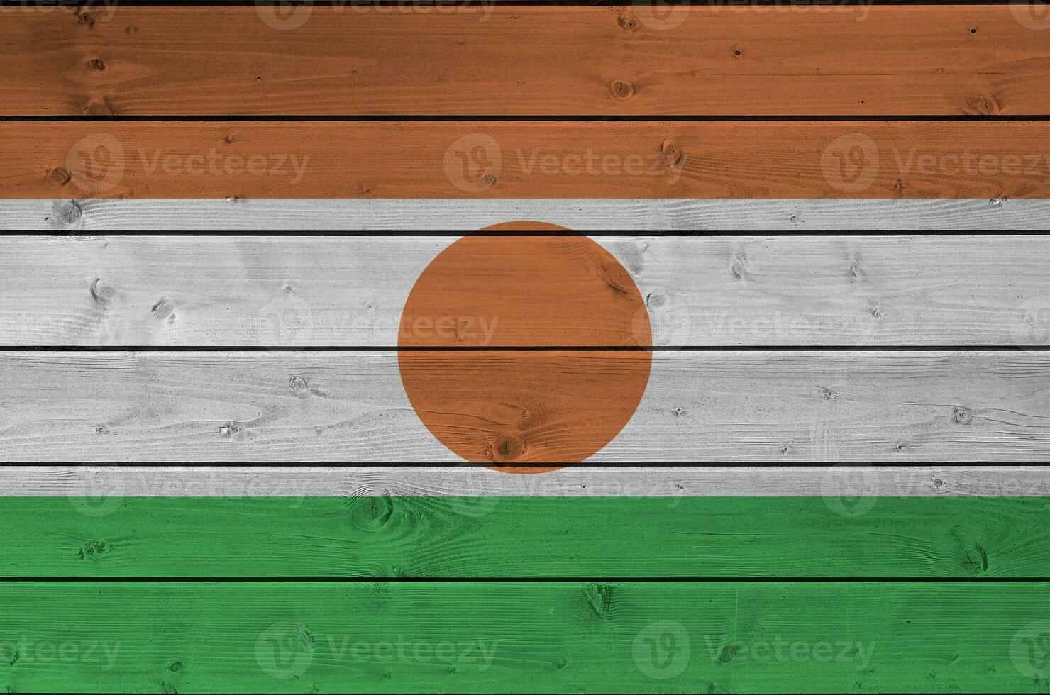 Niger flag depicted in bright paint colors on old wooden wall. Textured banner on rough background photo