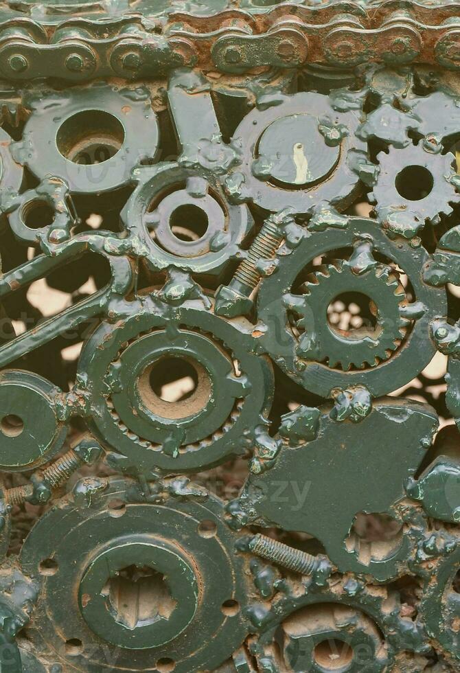 A composition of a set of gears and car parts that are welded to each other and painted green. Grunge steampunk texture photo