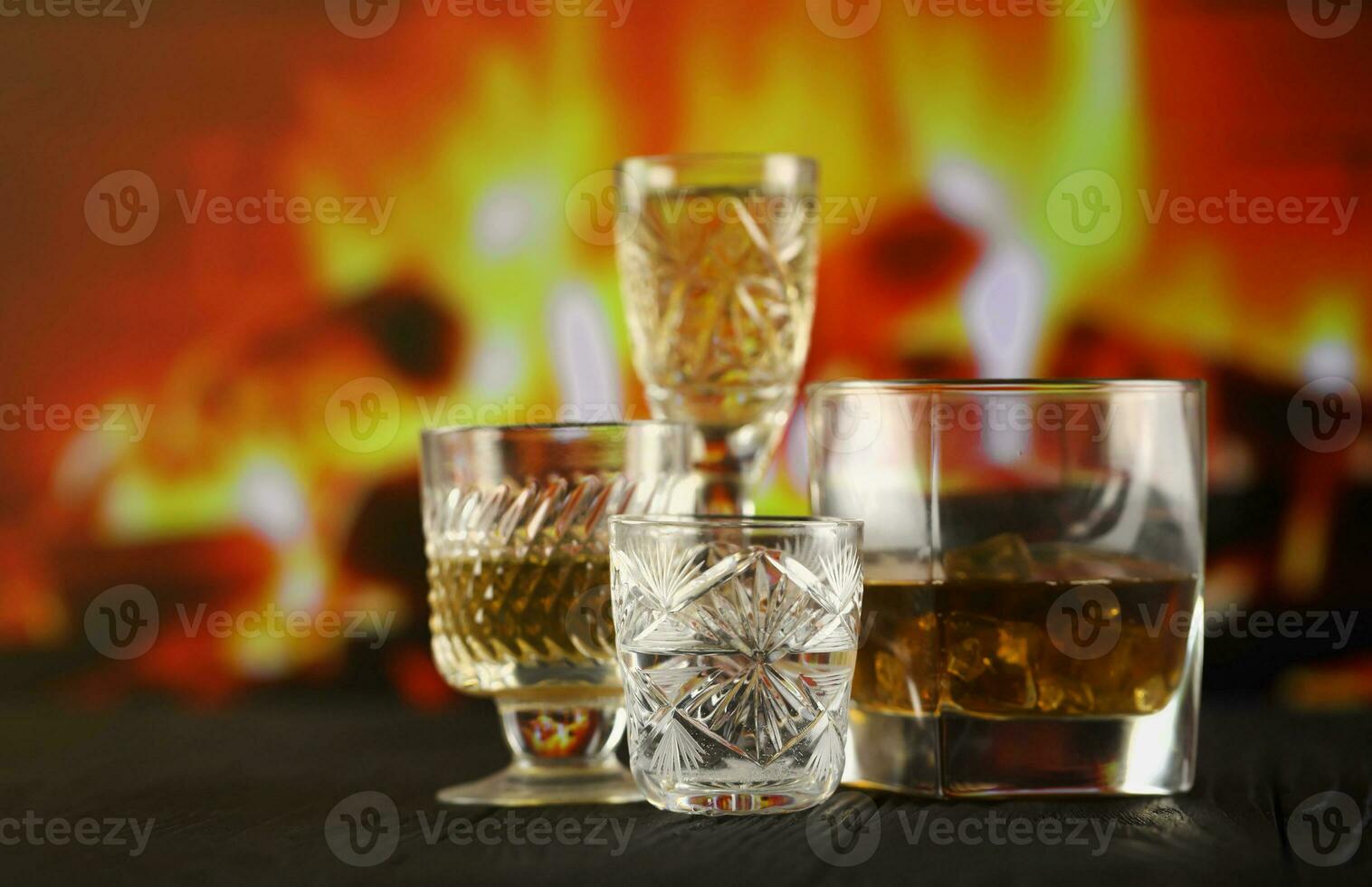 Different alcohol drinks in glass on wooden surface on fireplace background. Luxury elite alcohol in glass cups. Low key scene photo