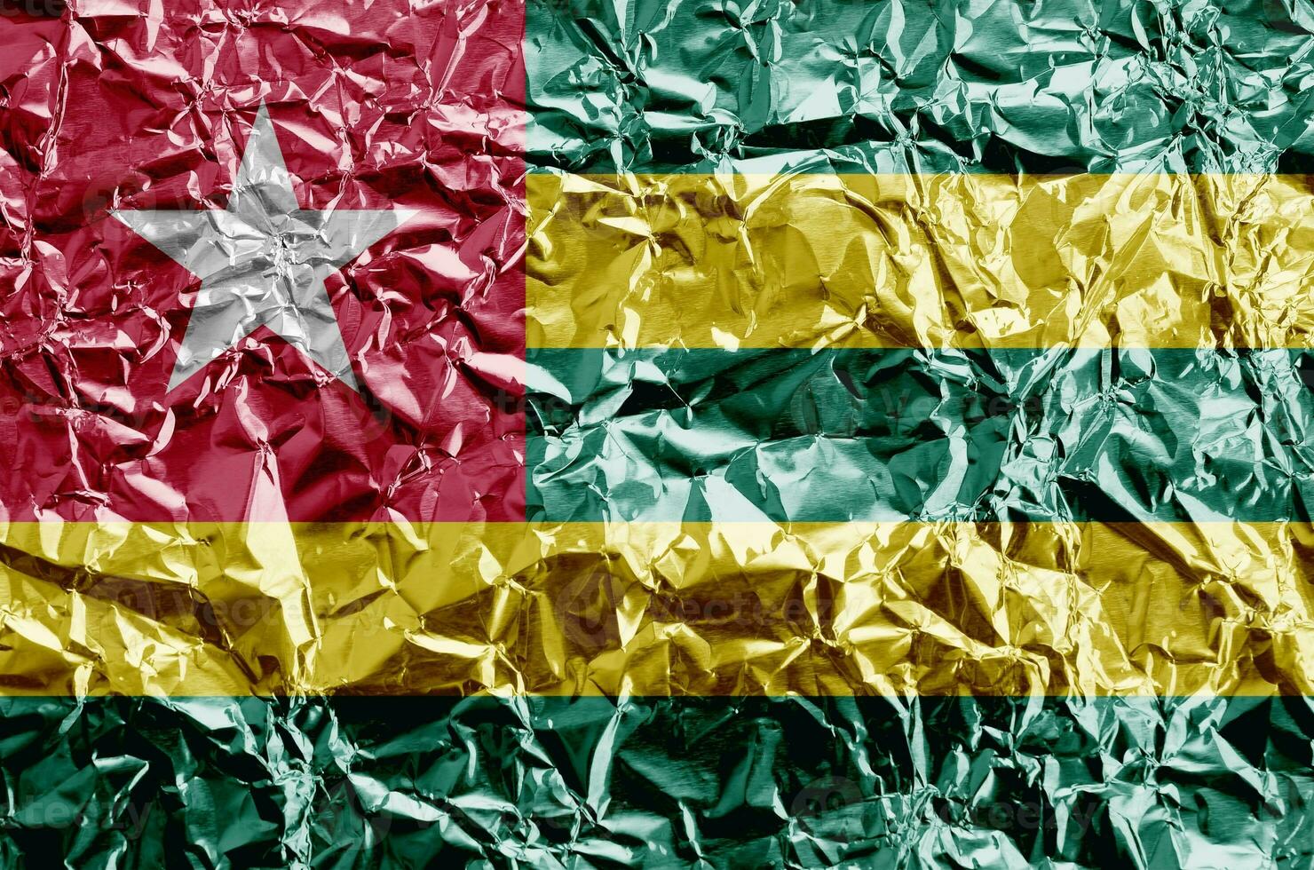 Togo flag depicted in paint colors on shiny crumpled aluminium foil closeup. Textured banner on rough background photo