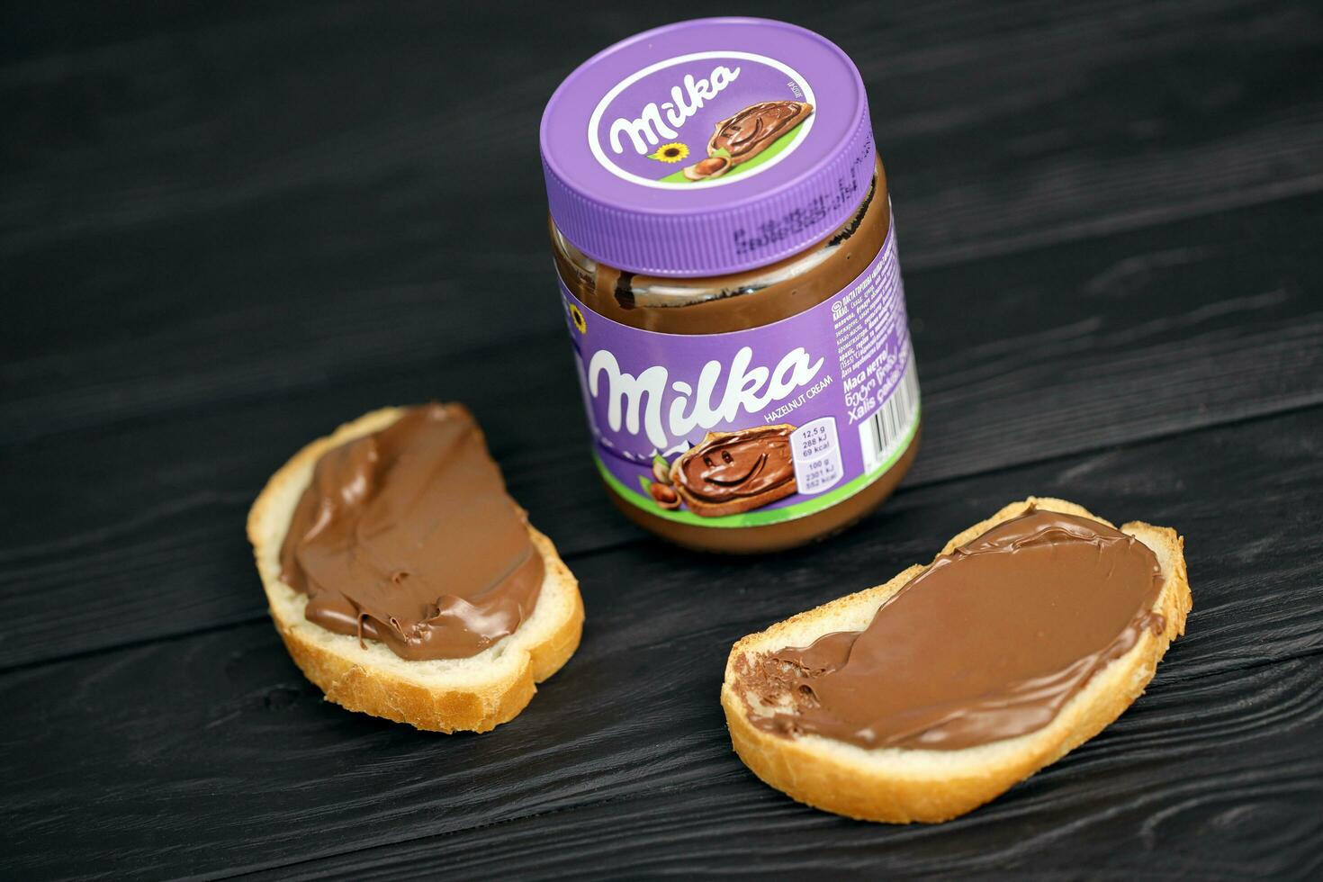 KHARKOV, UKRAINE - JULY 2, 2021 Can of Milka sweetened hazelnut cocoa spread with classical lilac color design on black table photo