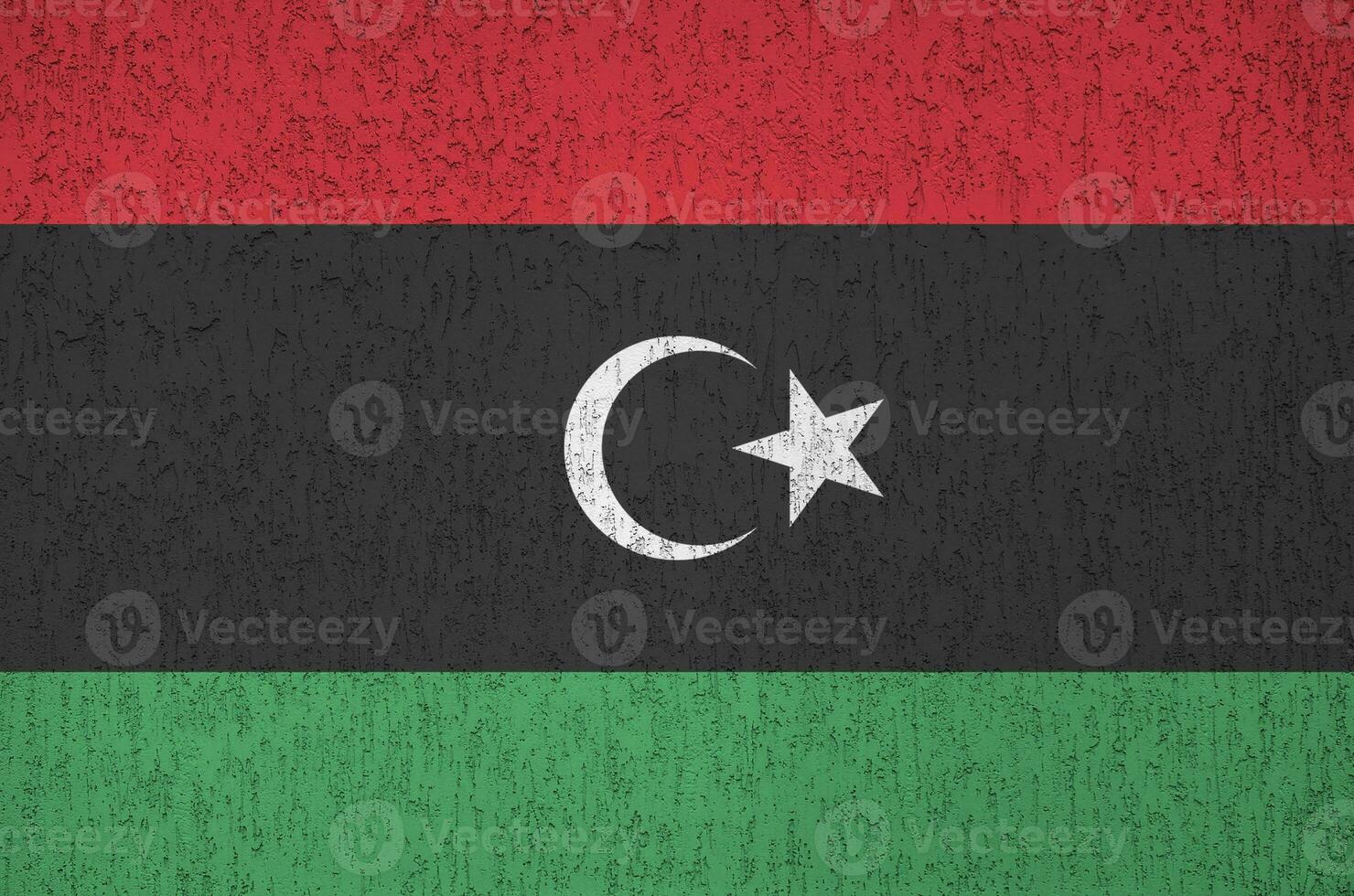 Libya flag depicted in bright paint colors on old relief plastering wall. Textured banner on rough background photo