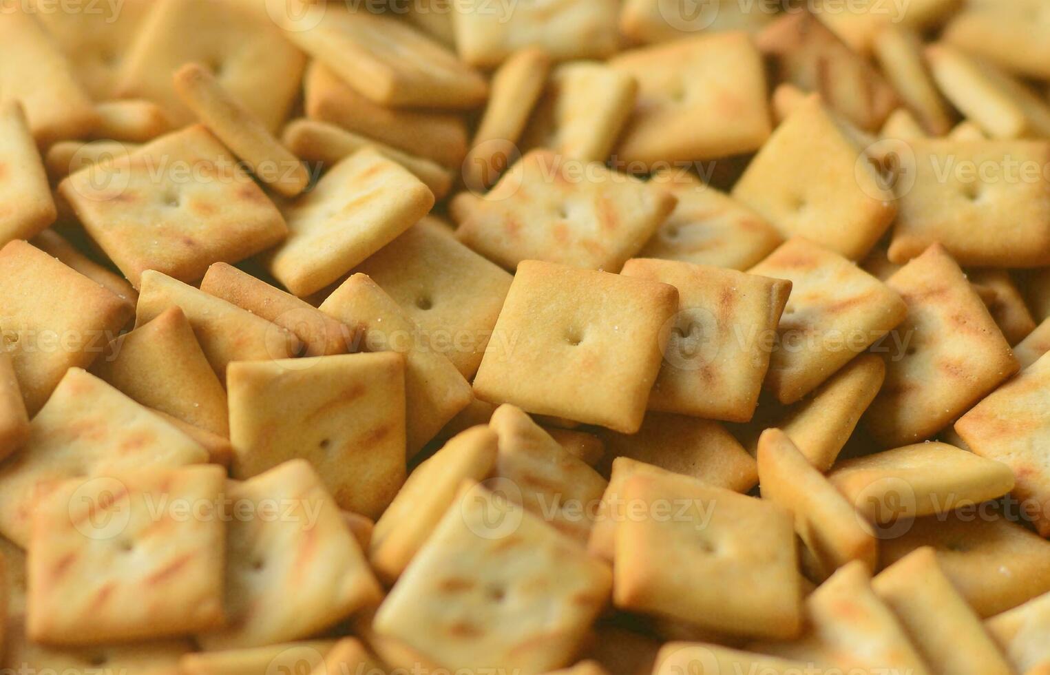 A lot of small cookies are square shaped. A pattern of a yellow salt cracker. Background image with salted pastry photo