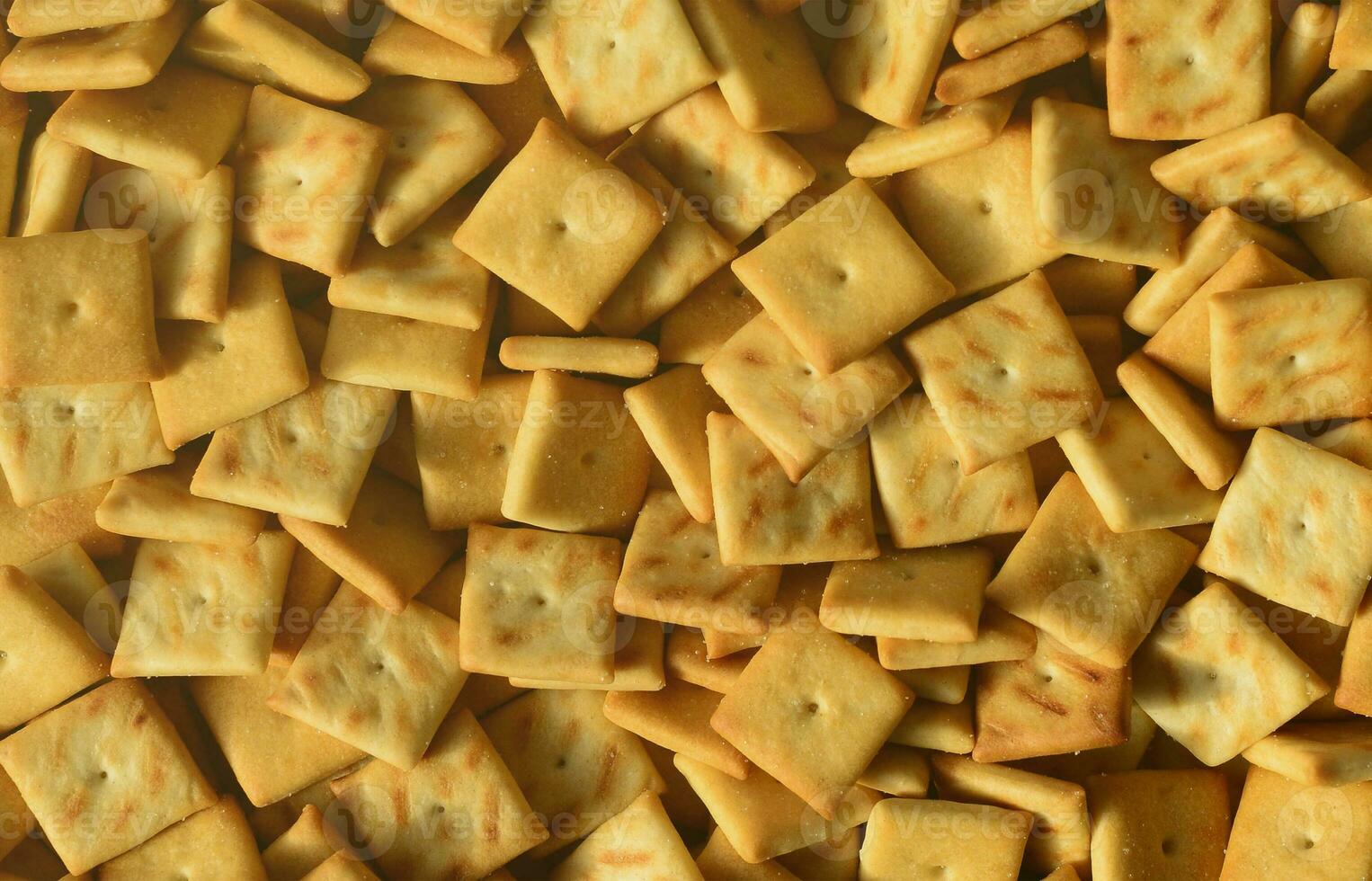 A lot of small cookies are square shaped. A pattern of a yellow salt cracker. Background image with salted pastry photo