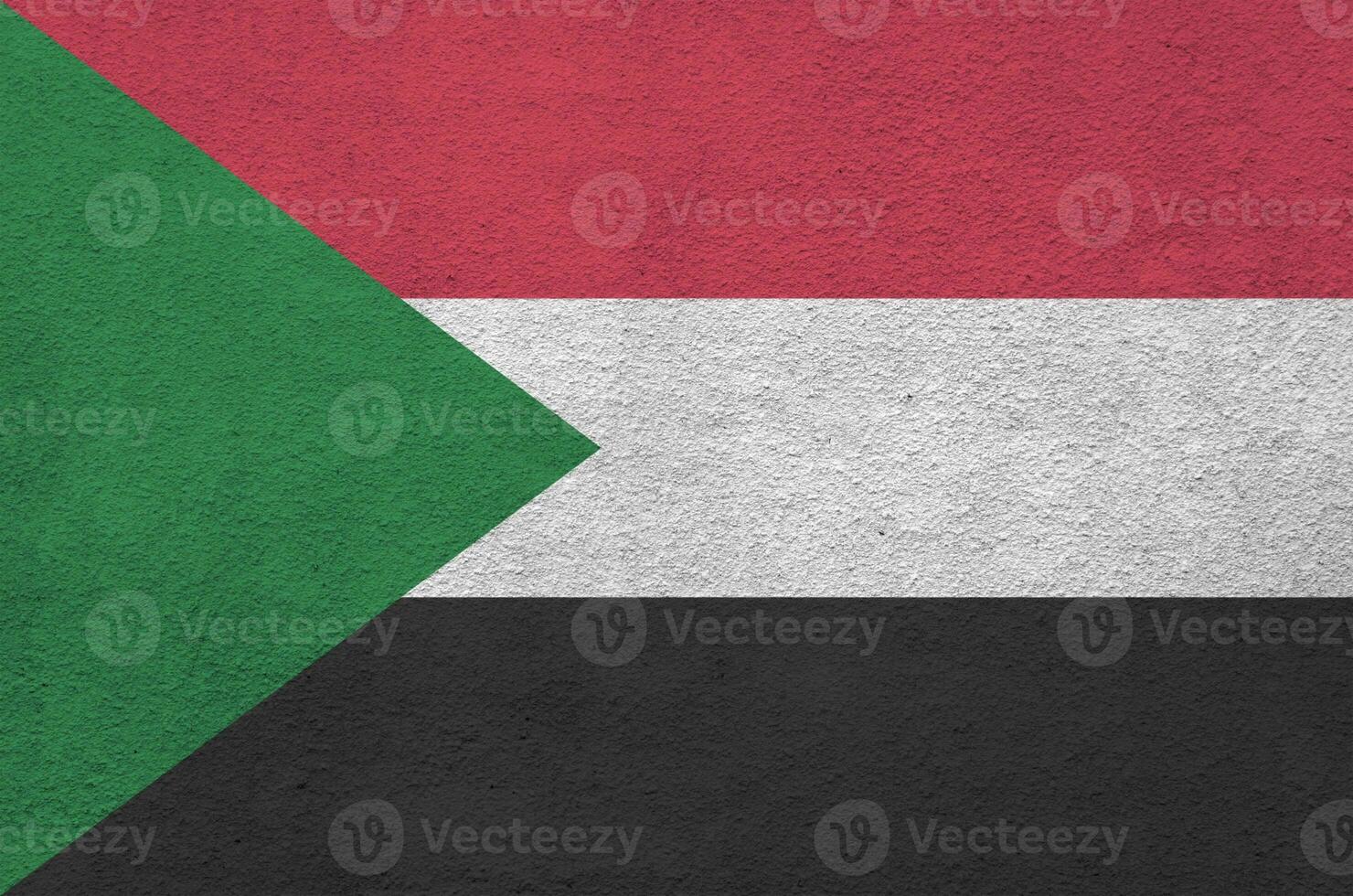 Sudan flag depicted in bright paint colors on old relief plastering wall. Textured banner on rough background photo