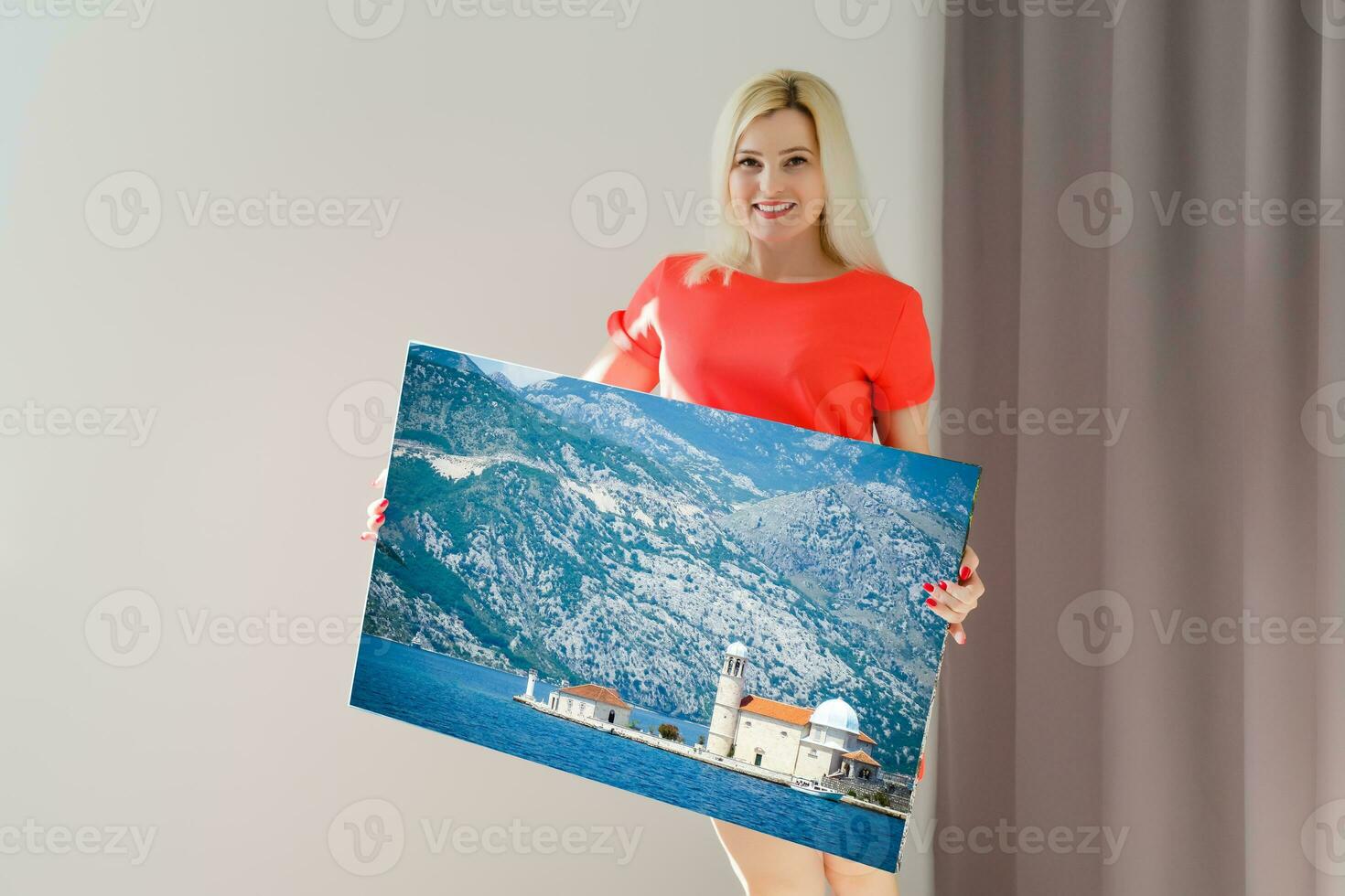 A happy young blonde woman is holding a large wall photo canvas at home