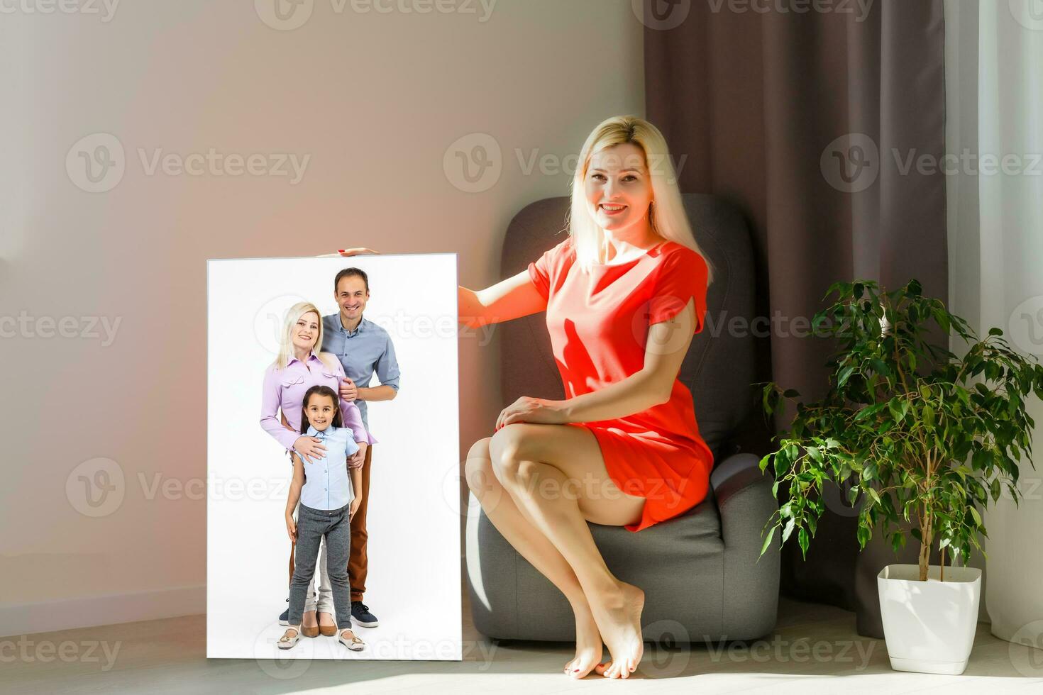 A happy young blonde woman is holding a large wall canvas at home photo