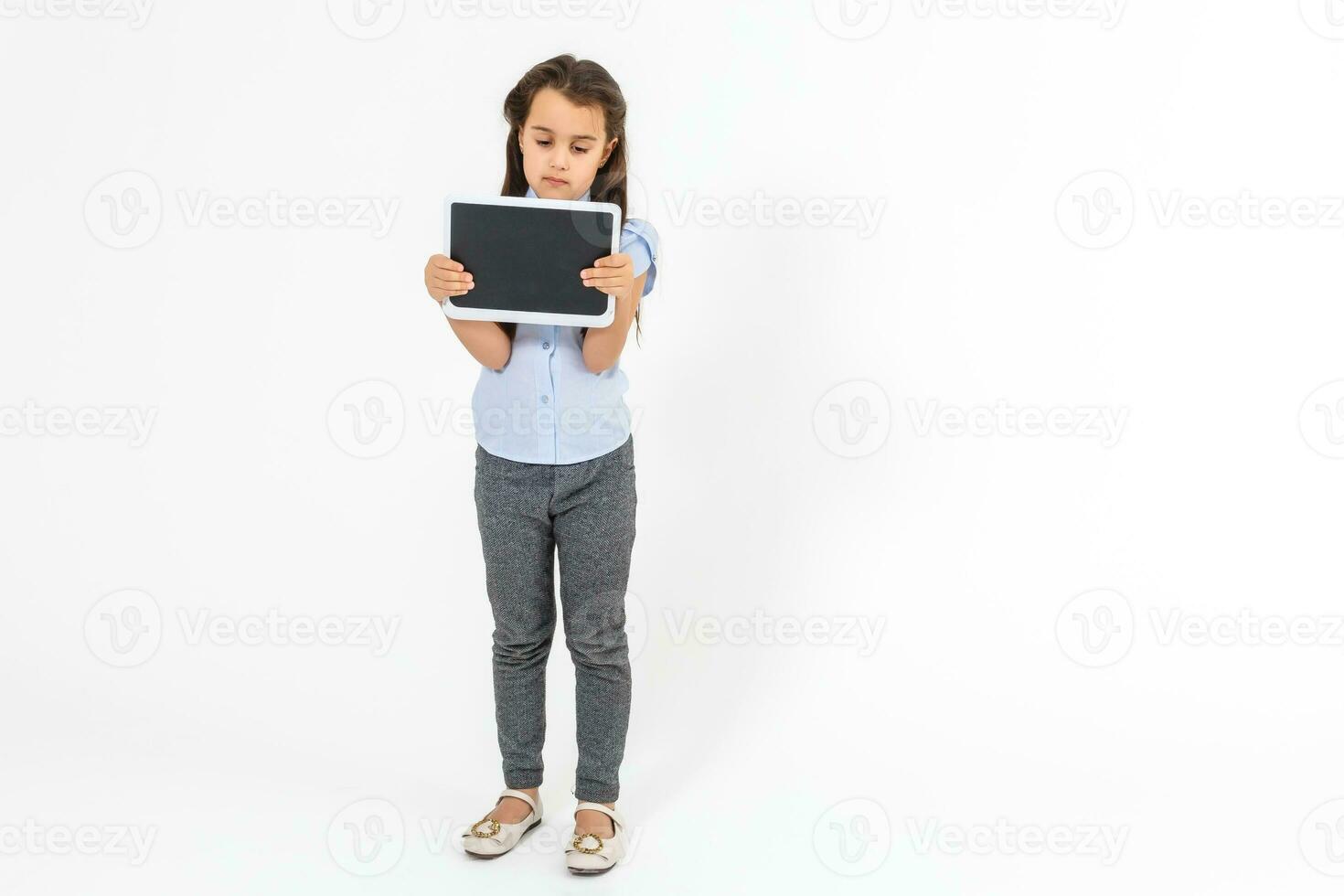 School and technology. Full length of pretty little girl standing with backpack holding tablet computer. Isolated on white. photo