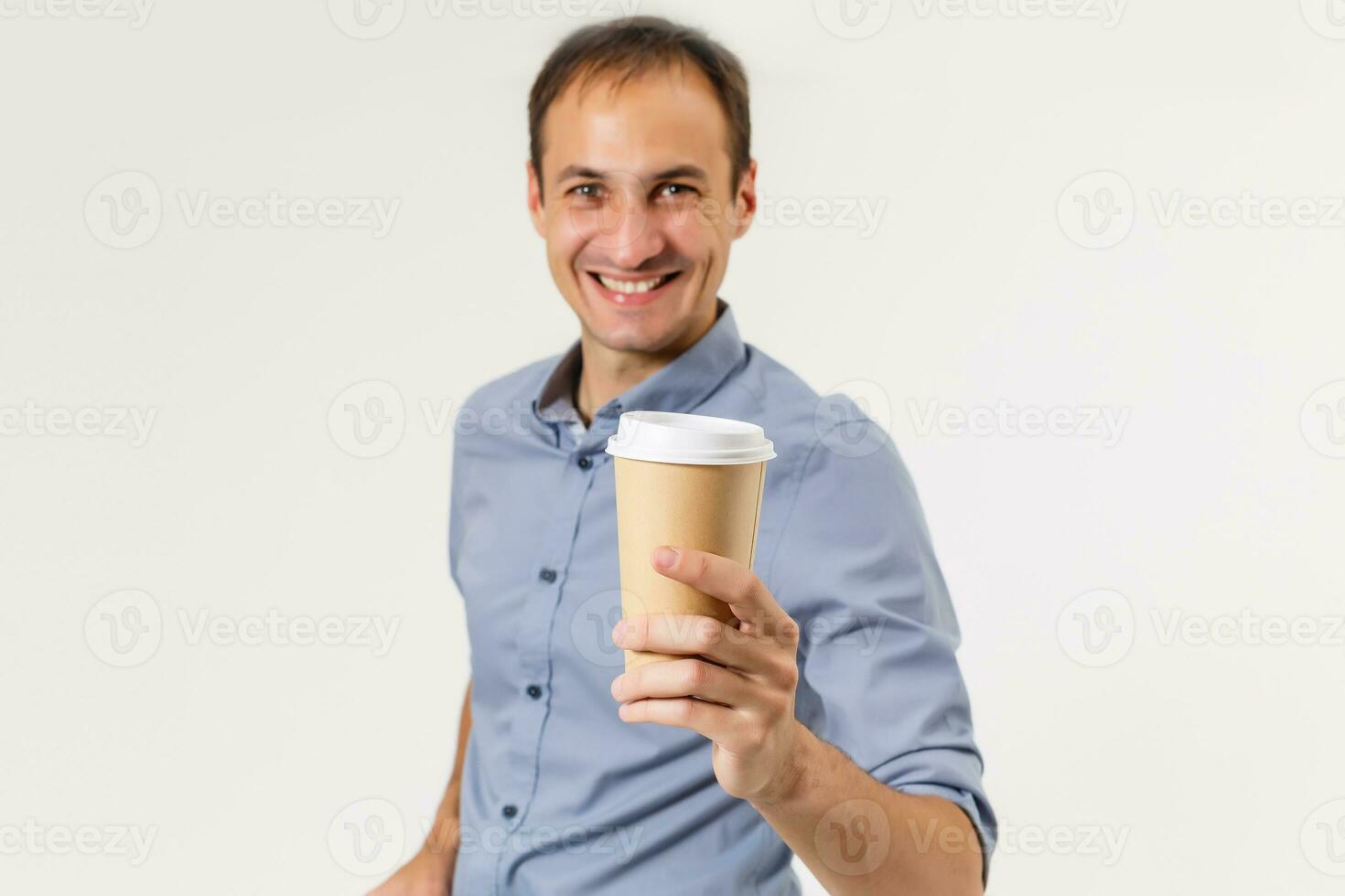 Happy young man in a shirt holds a cup of coffee in his hands, looks into the camera and smiles, isolated on a white background. photo