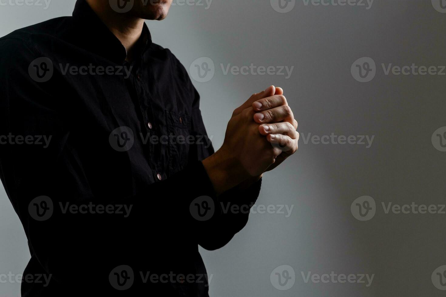 hombre guapo sentarse oración sobre fondo negro. sus manos están orando por las bendiciones de dios. foto