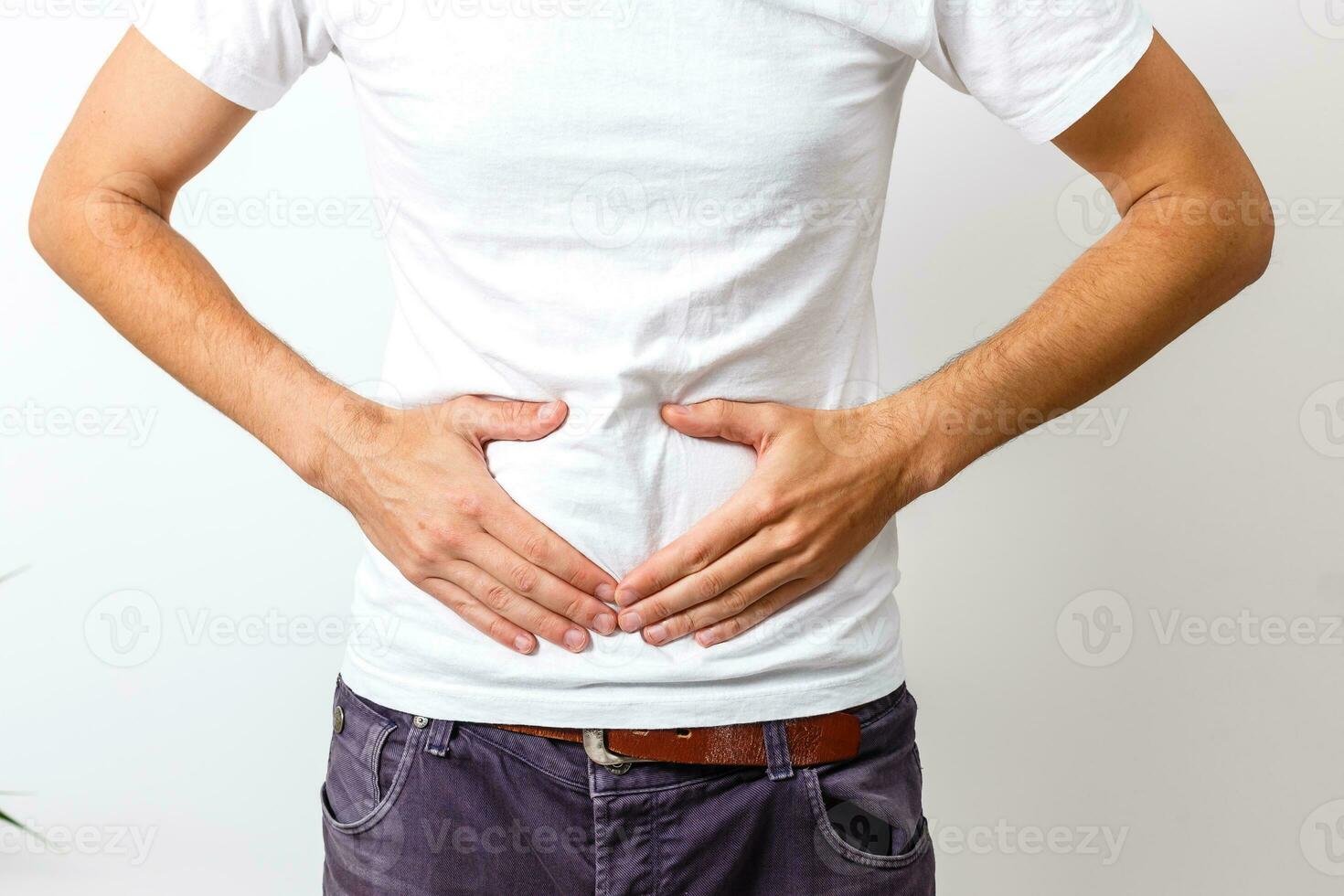 Young handsome man wearing white t-shirt over isolated background with hand on stomach because nausea, painful disease feeling unwell. Ache concept. photo