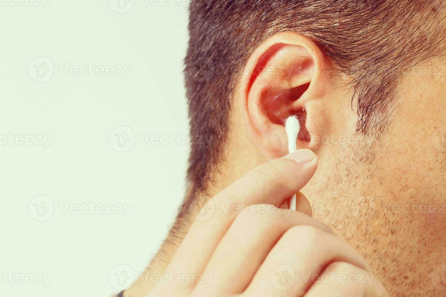A young man cleans dirty ears with a white cotton swab on a white background. Medical sterile cotton swab in a man's hand close-up. photo