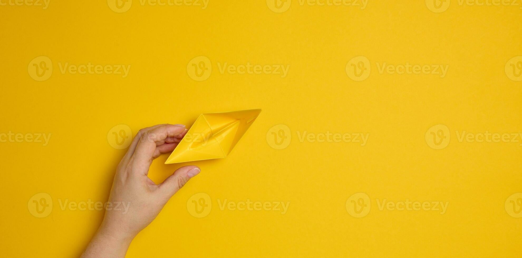Female hand hold a blue paper boat on a yellow background. Mentoring and support concept photo