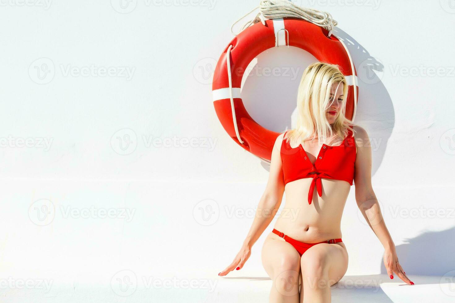 retrato de sonriente moderno mujer en rojo trajes de baño en el litoral demostración inflable boya salvavidas foto