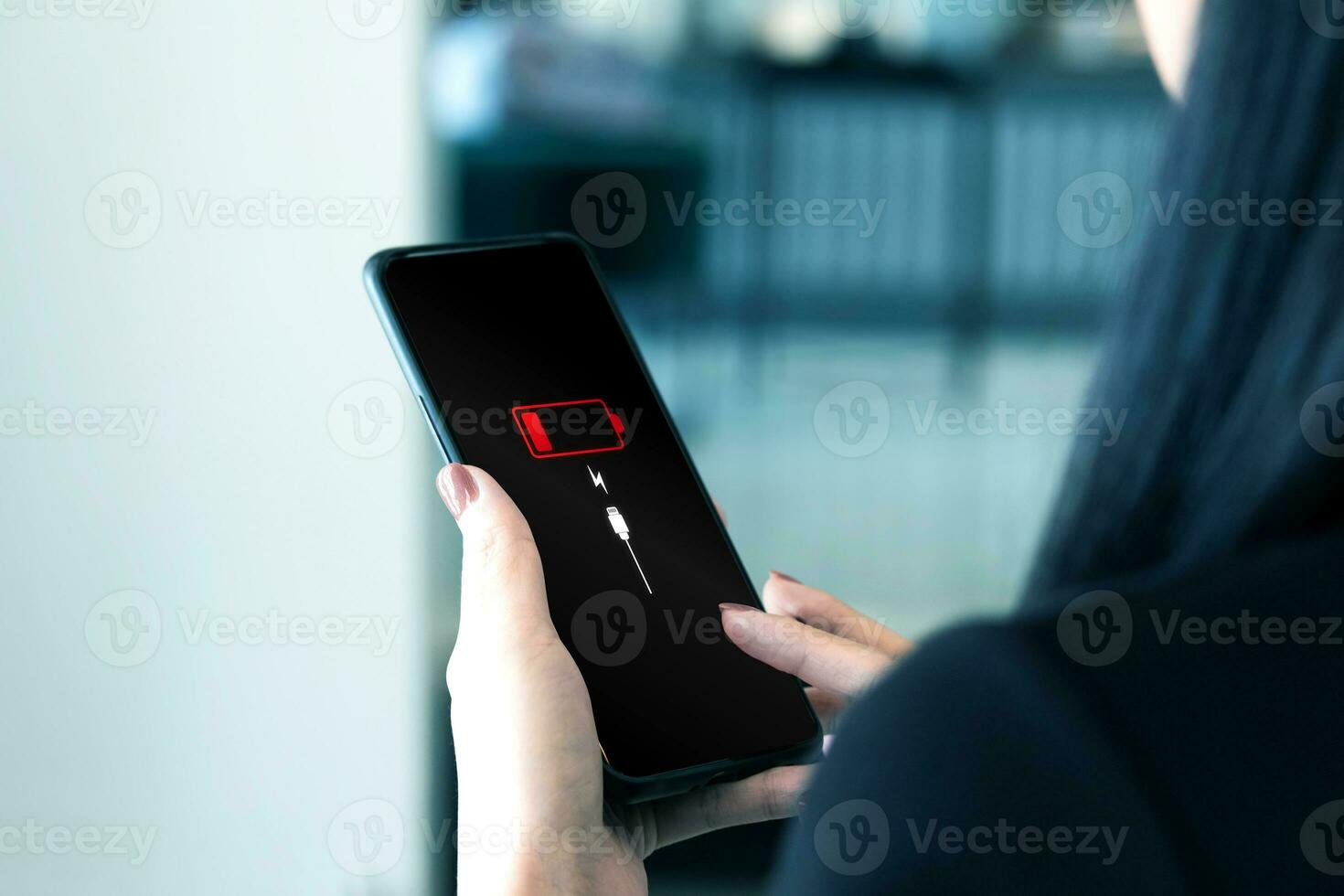 Close up view of woman holding smartphone with low battery symbol notification on the screen. Battery power and plugging the charger into your smartphone with a power backup charger photo