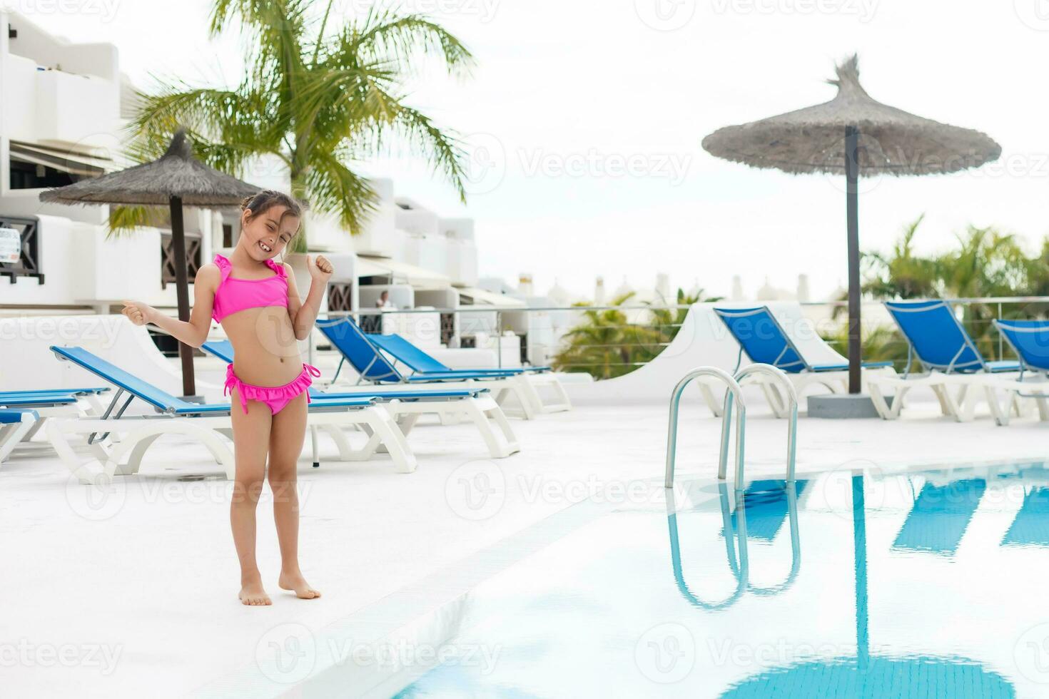 Beautiful little girl spread her arms standing near swimming pool photo