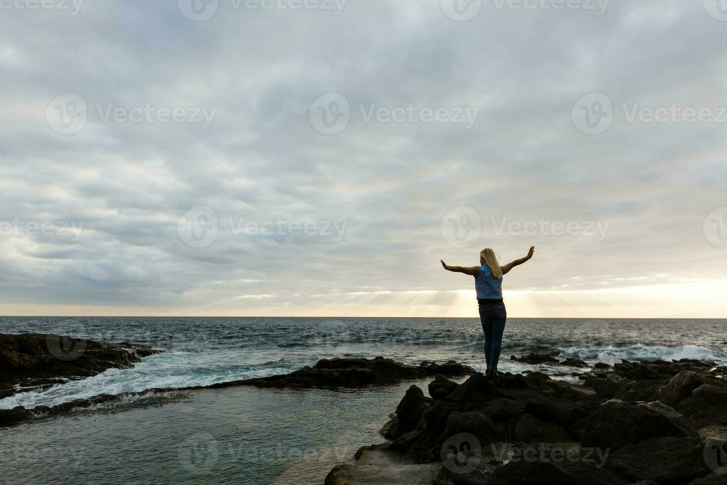 Women on volcanic rocks and blue ocean with waves, white foam and volcanic rocks. Canary Islands. The magnificent coast of the Atlantic Ocean photo