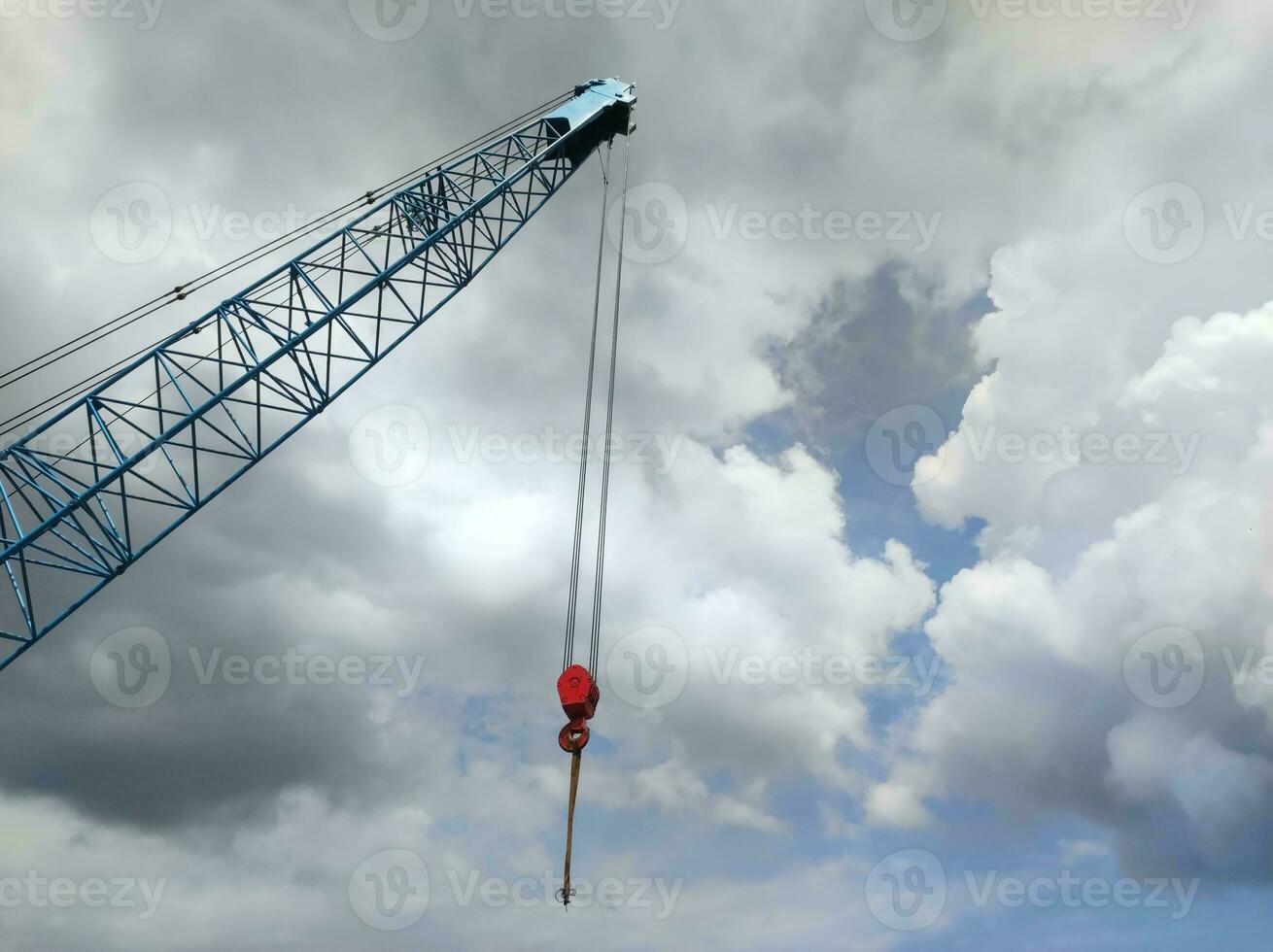 Selective focus on hook hanging on crane boom against bright blue and cloudy sky background photo