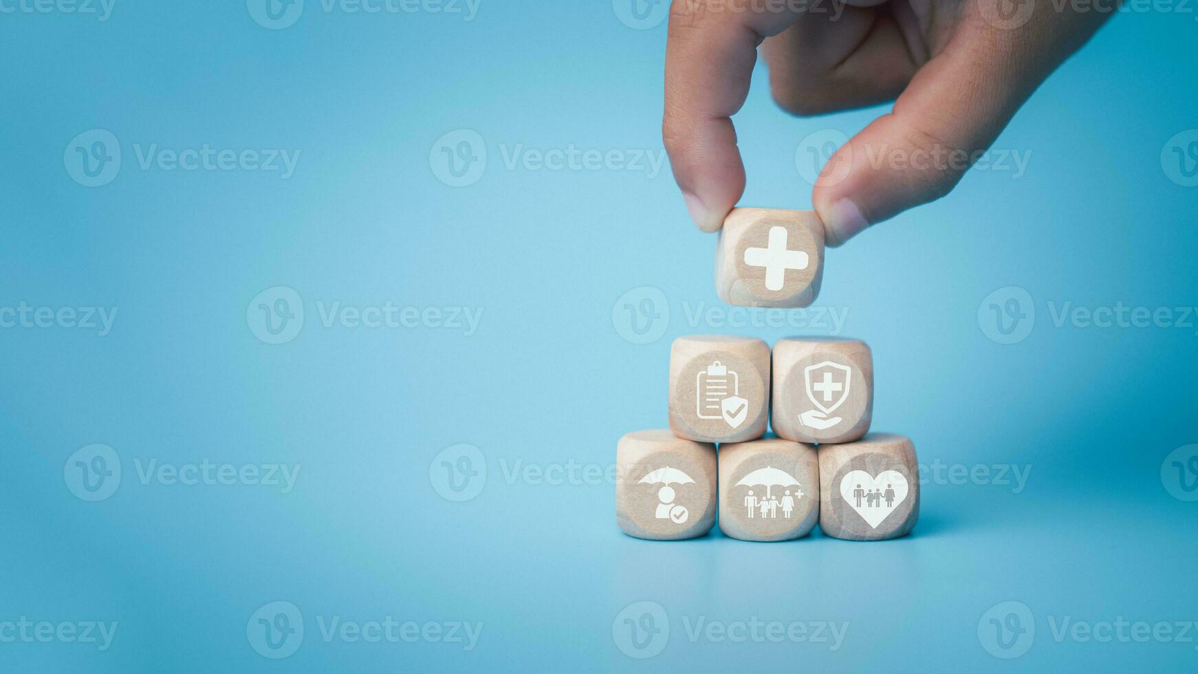 Health insurance and healthcare concept, human hand holds wooden block with icons about health insurance and healthcare access, retirement planning on blue background. photo