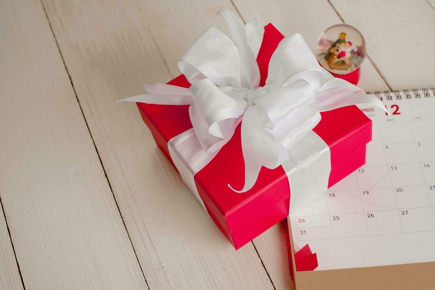 Red gift box on calendar isolated on white wooden background with. Christmas's day concept. Planning scheduling agenda, Event, organiser x'mas day. Flat lay, top view. photo